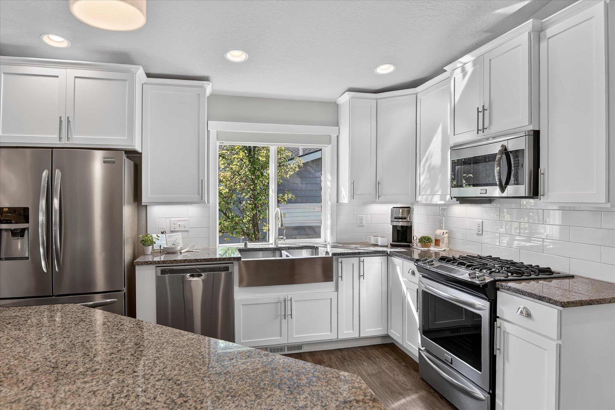 Bright kitchen with white cabinets, granite counters, farmhouse sink, and stainless steel appliances.