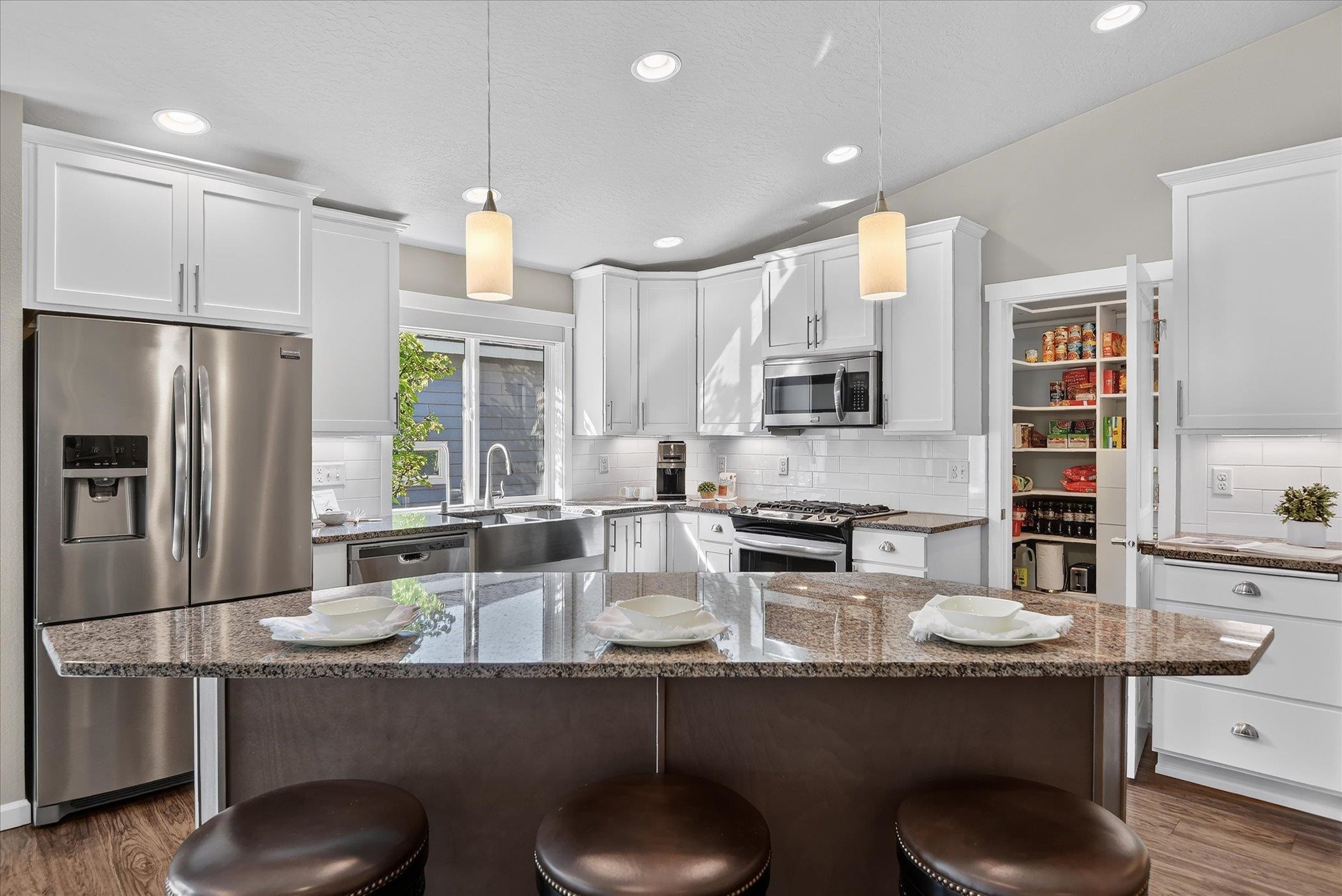 Bright kitchen with white cabinets, stainless steel appliances, and a granite island with three stools.