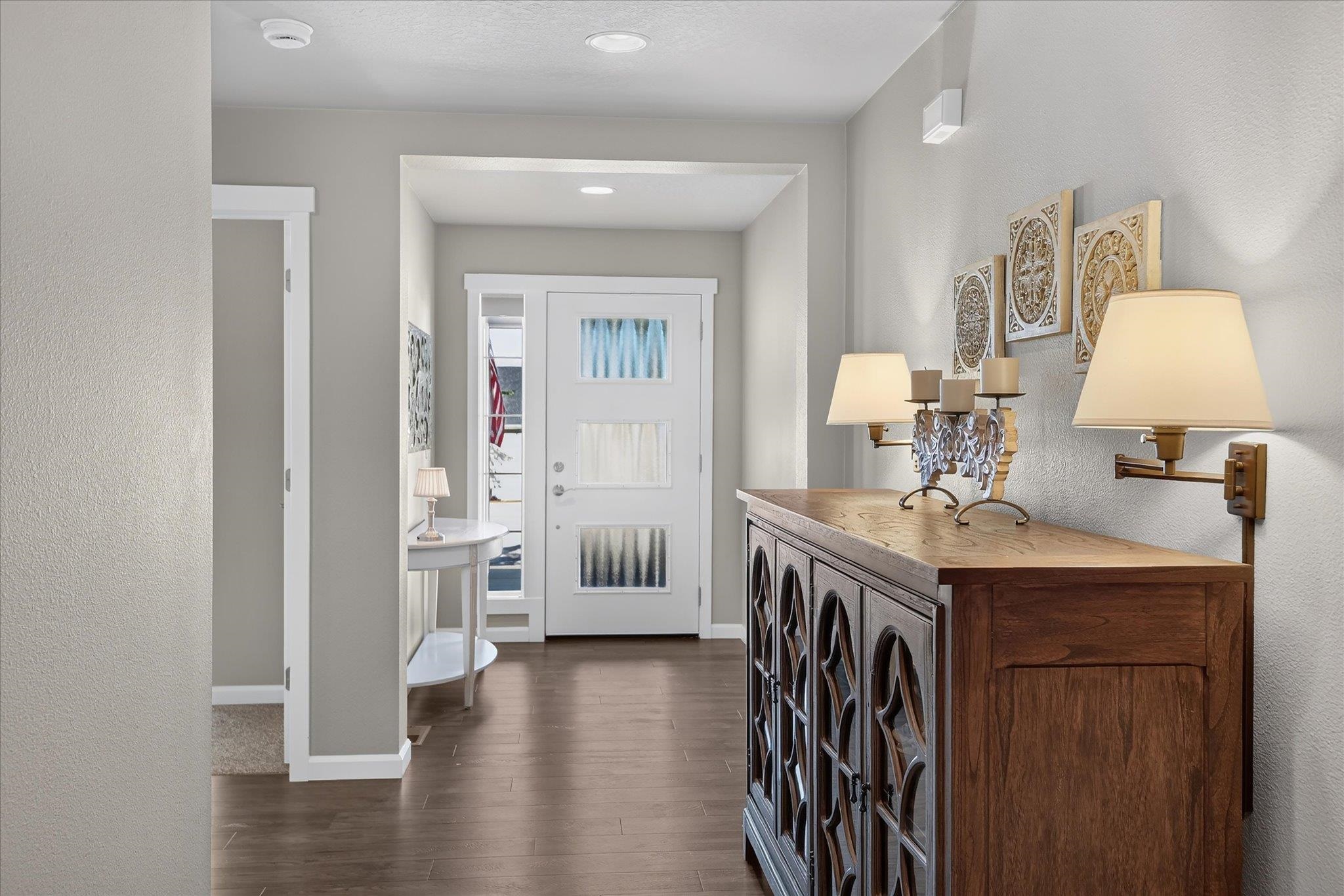 Entryway with a white front door, dark wood floors, and a carved wooden console with lamps.
