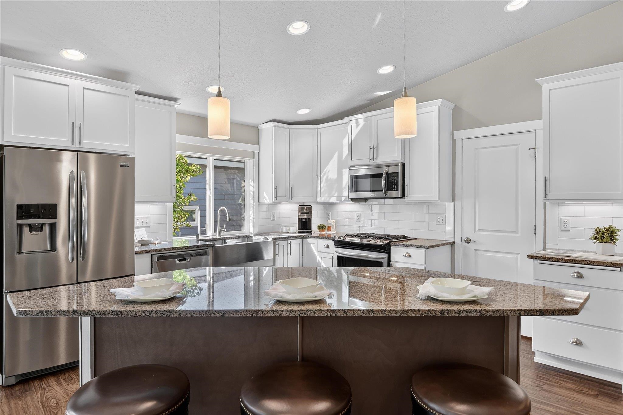 Bright kitchen with white cabinets, stainless appliances, and a granite island with three stools.