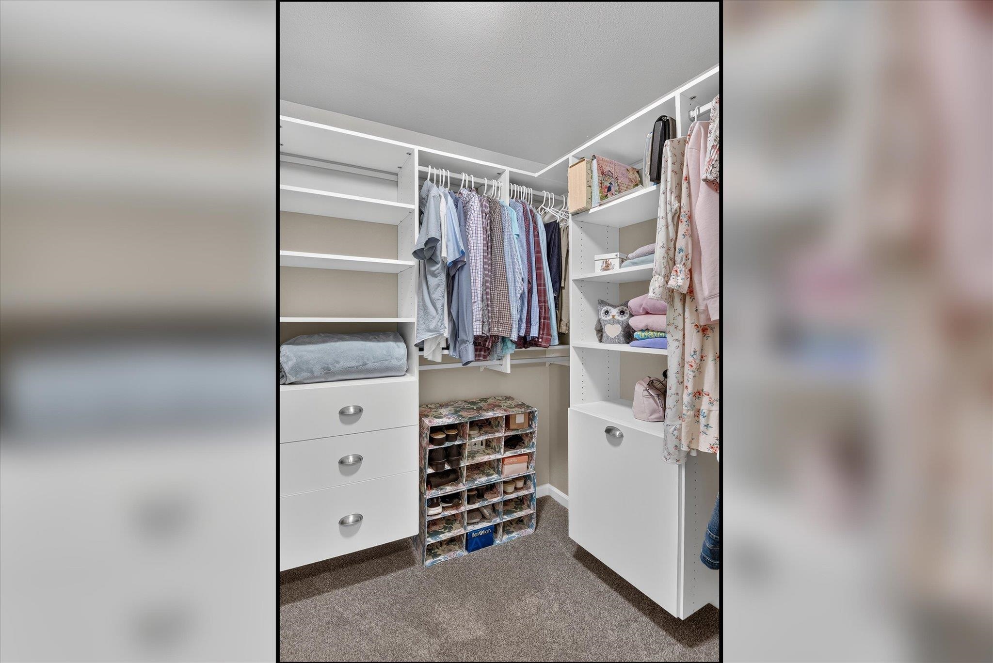Walk-in closet with built-in white shelves, hanging clothes, and shoe cubbies.