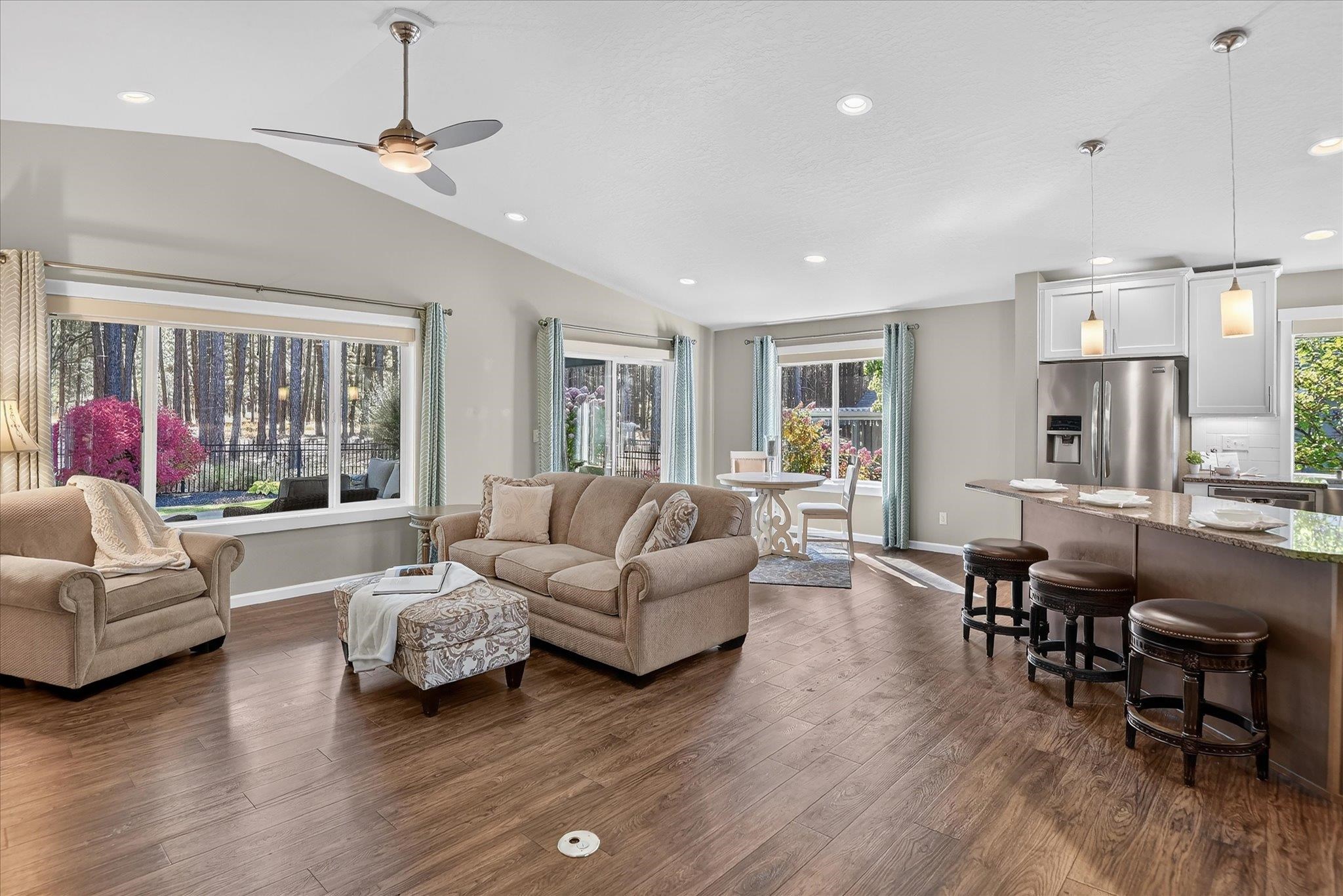 Open-plan living room and kitchen with wood floors, an island, and large windows overlooking trees.