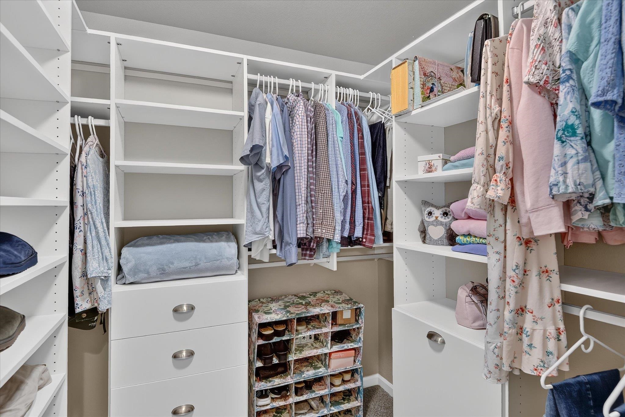 Walk-in closet with white built-in shelves, hanging clothes, drawers, and a shoe organizer.