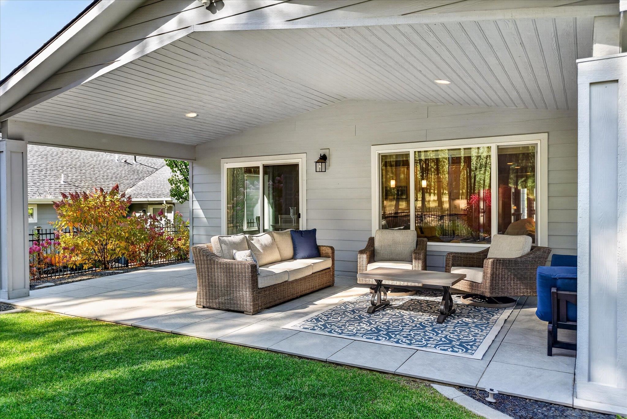 Covered patio with wicker seating, a patterned rug, and sliding glass doors beside the lawn.