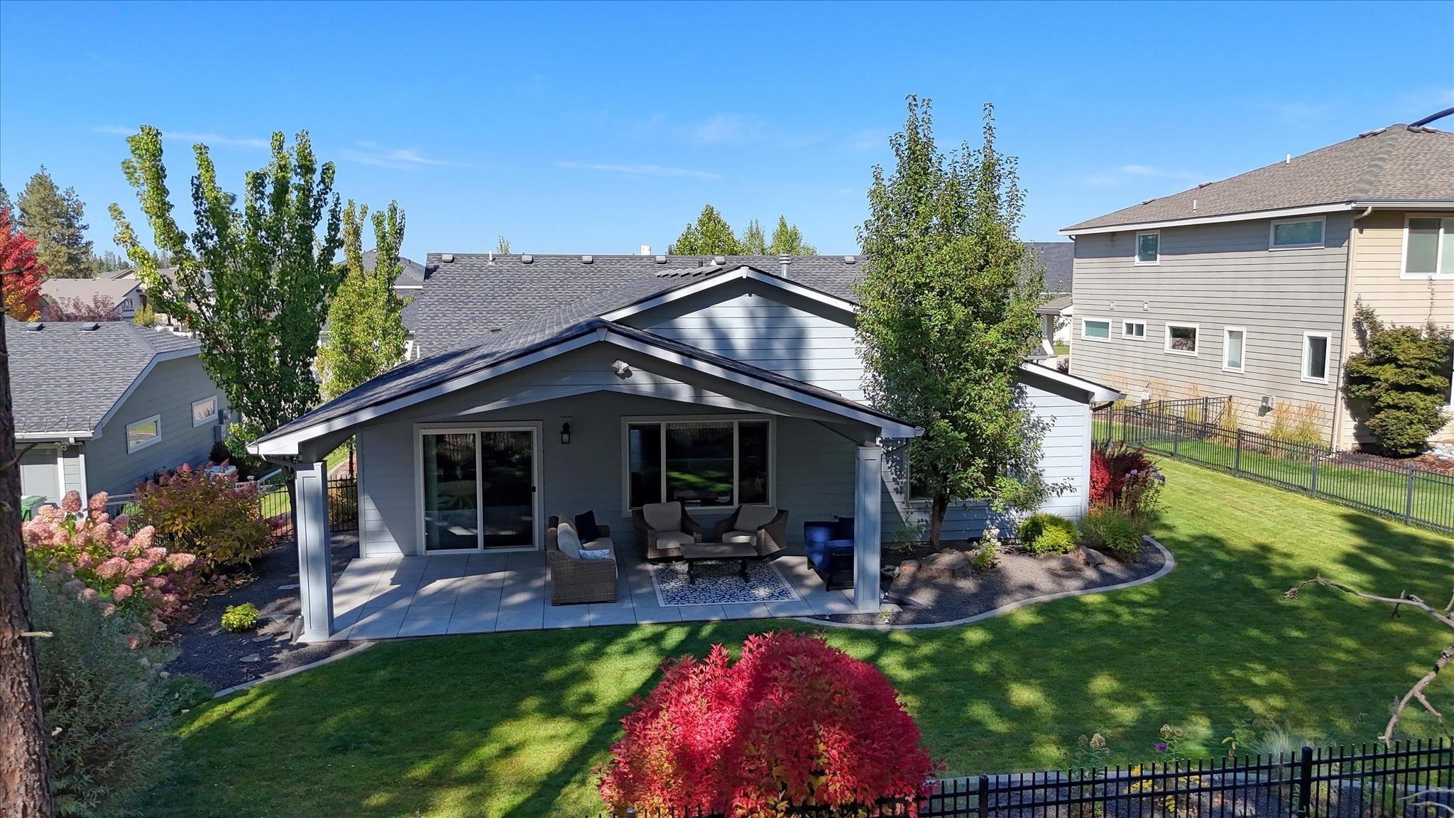 Gray home with a furnished covered patio overlooking a landscaped backyard.