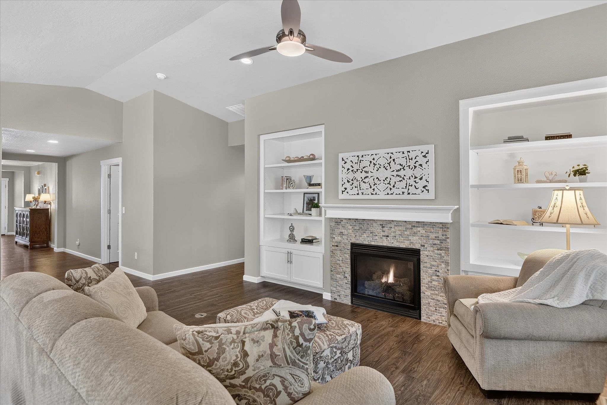 Furnished living room with a stone fireplace, built-in shelving, and vaulted ceiling.