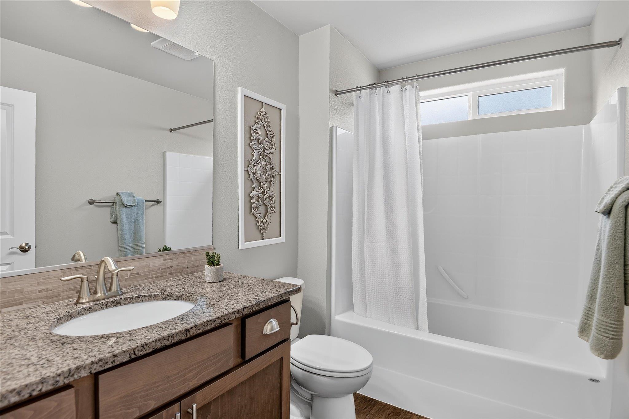 Bathroom with a granite-topped wood vanity beside a white tub and shower with a high window.