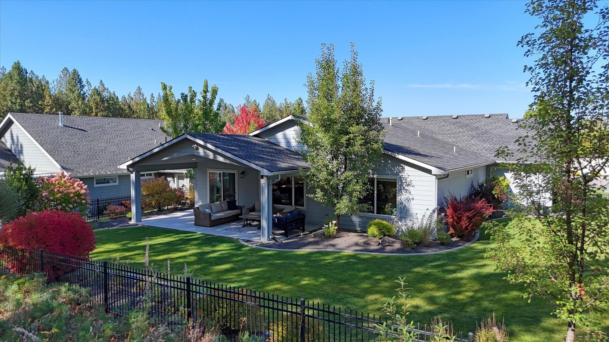 Home’s rear exterior with covered patio, outdoor seating, landscaped lawn, and black metal fence.
