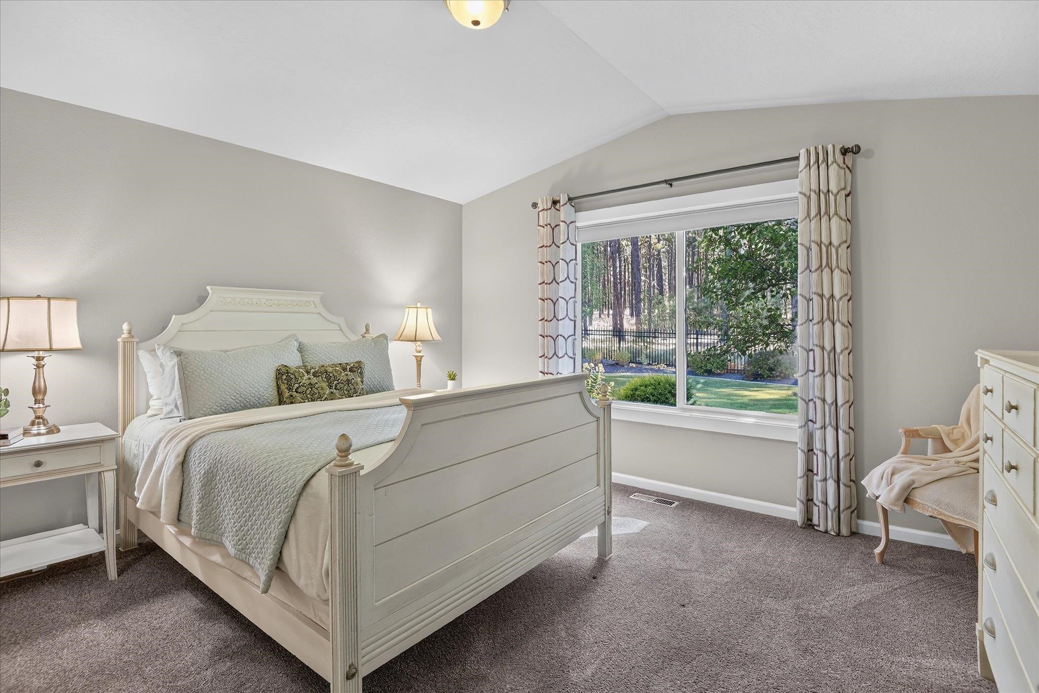 Staged bedroom with a white paneled bed and a large window overlooking a tree-lined yard.