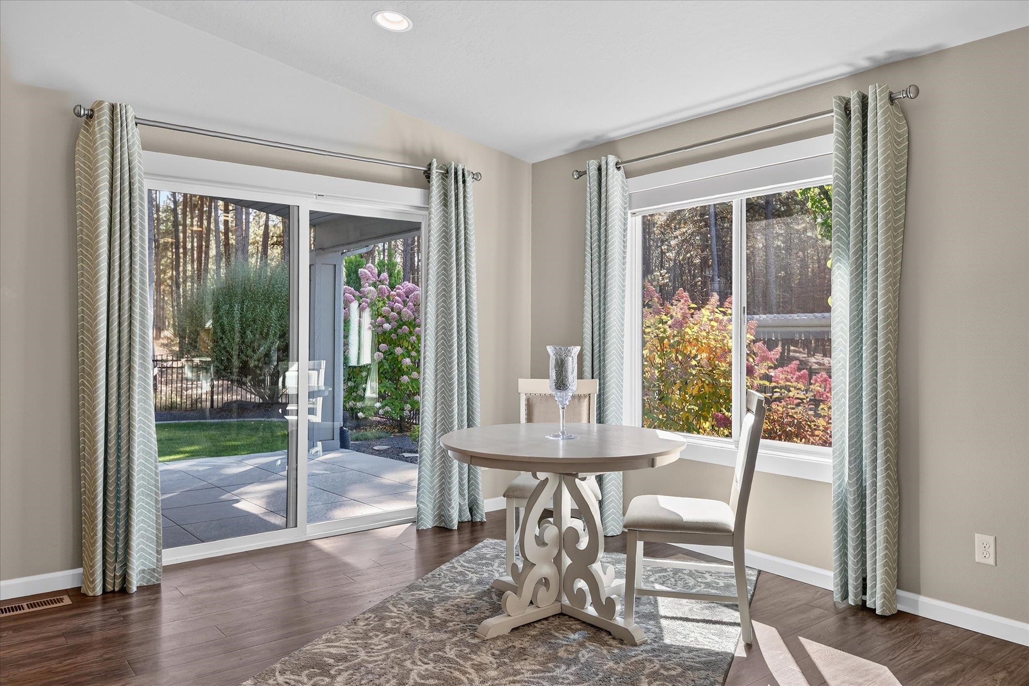 Dining nook with round table beside large windows and a sliding glass door overlooking a garden patio.