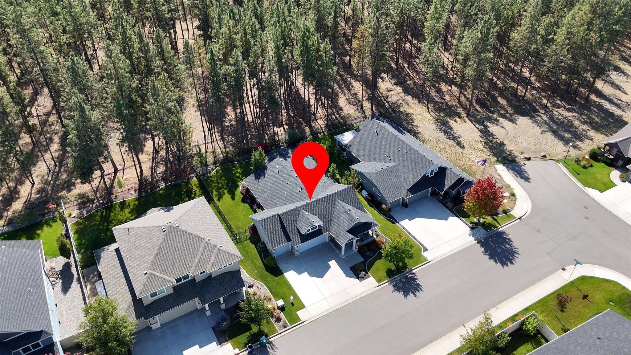 Aerial view of a gray-roofed house beside a wooded area, marked with a red location pin.