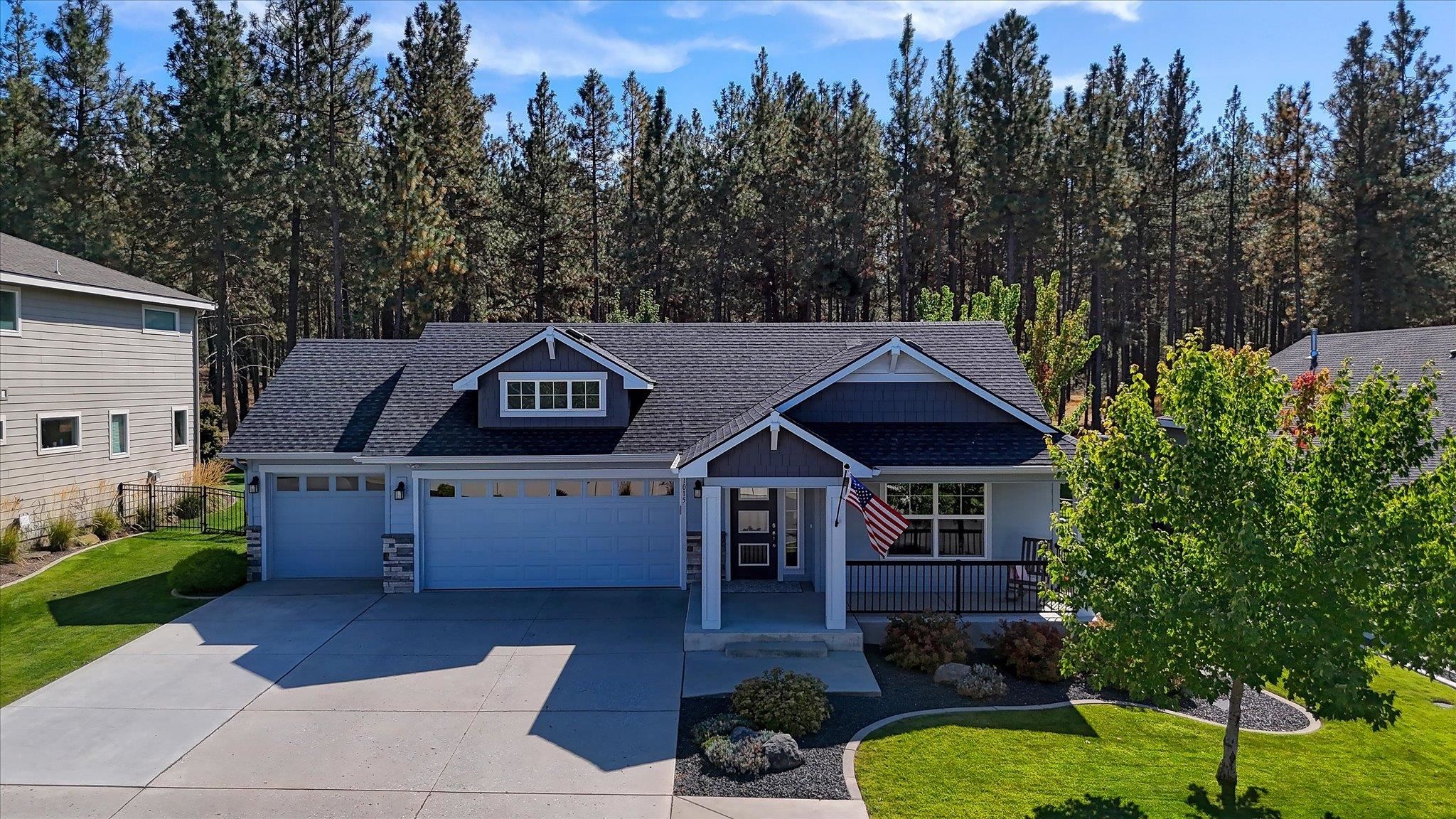 Blue-gray house with a double garage and covered entry, backed by tall pine trees.