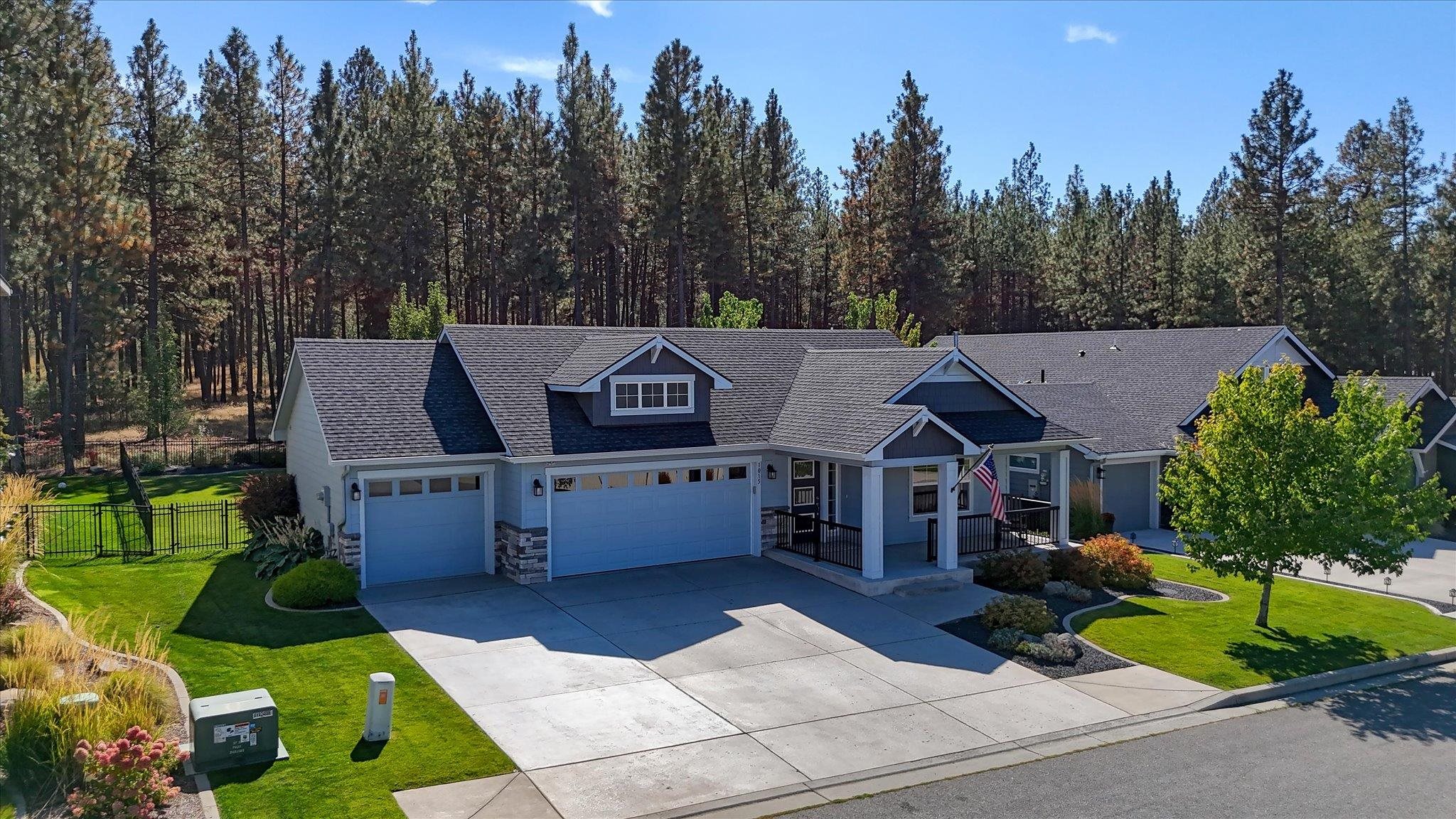 Blue-gray single-story home with multiple garage doors, a covered entry, and a lawn bordered by pine trees.