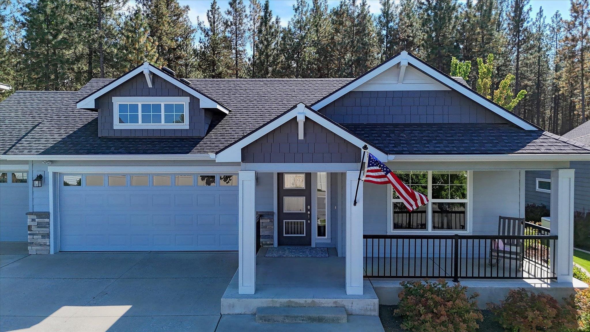 Blue-gray house with a two-car garage, covered porch, and American flag.