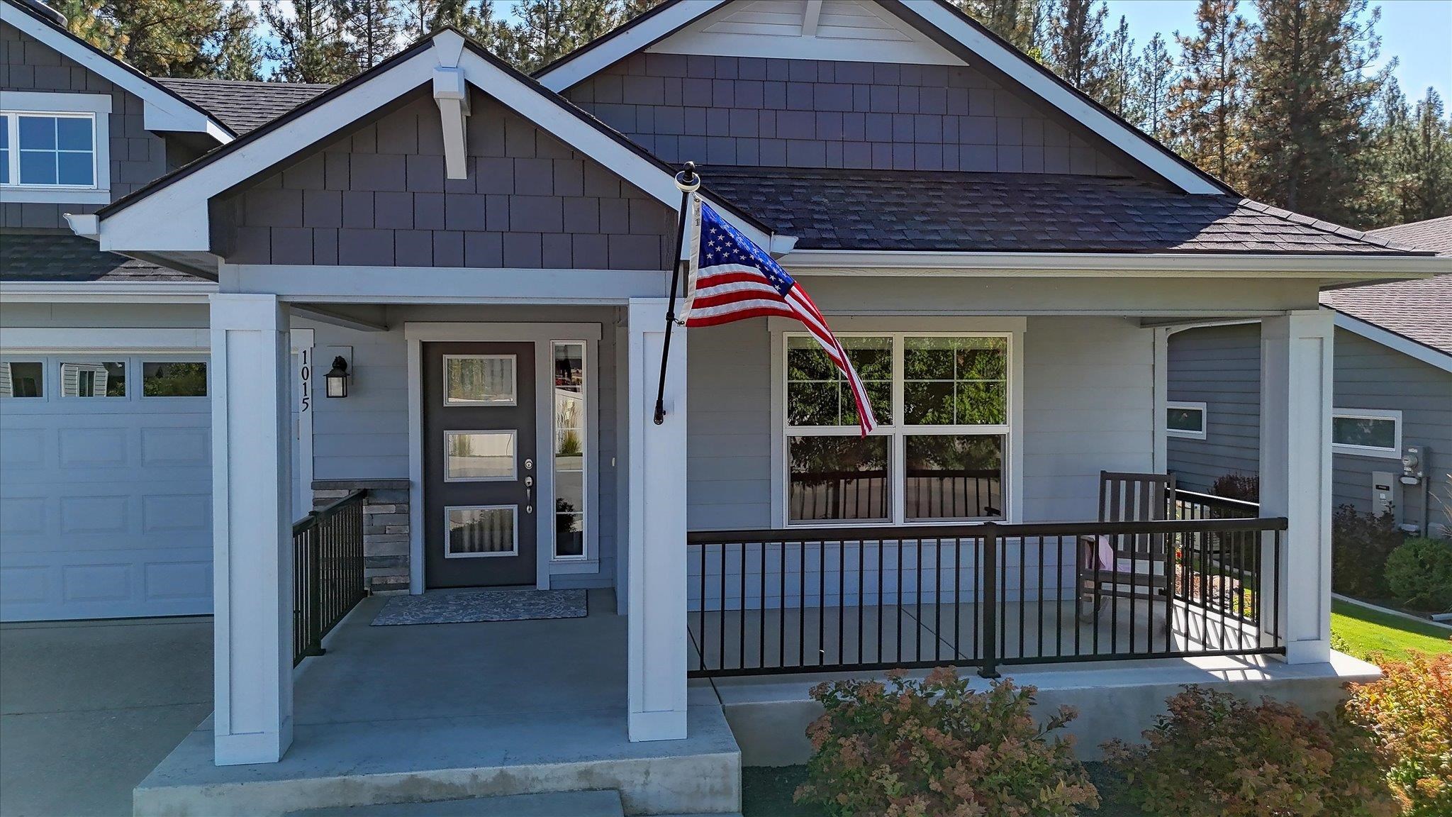 Blue-gray house with white trim, covered porch, attached garage, and an American flag by the front entrance.