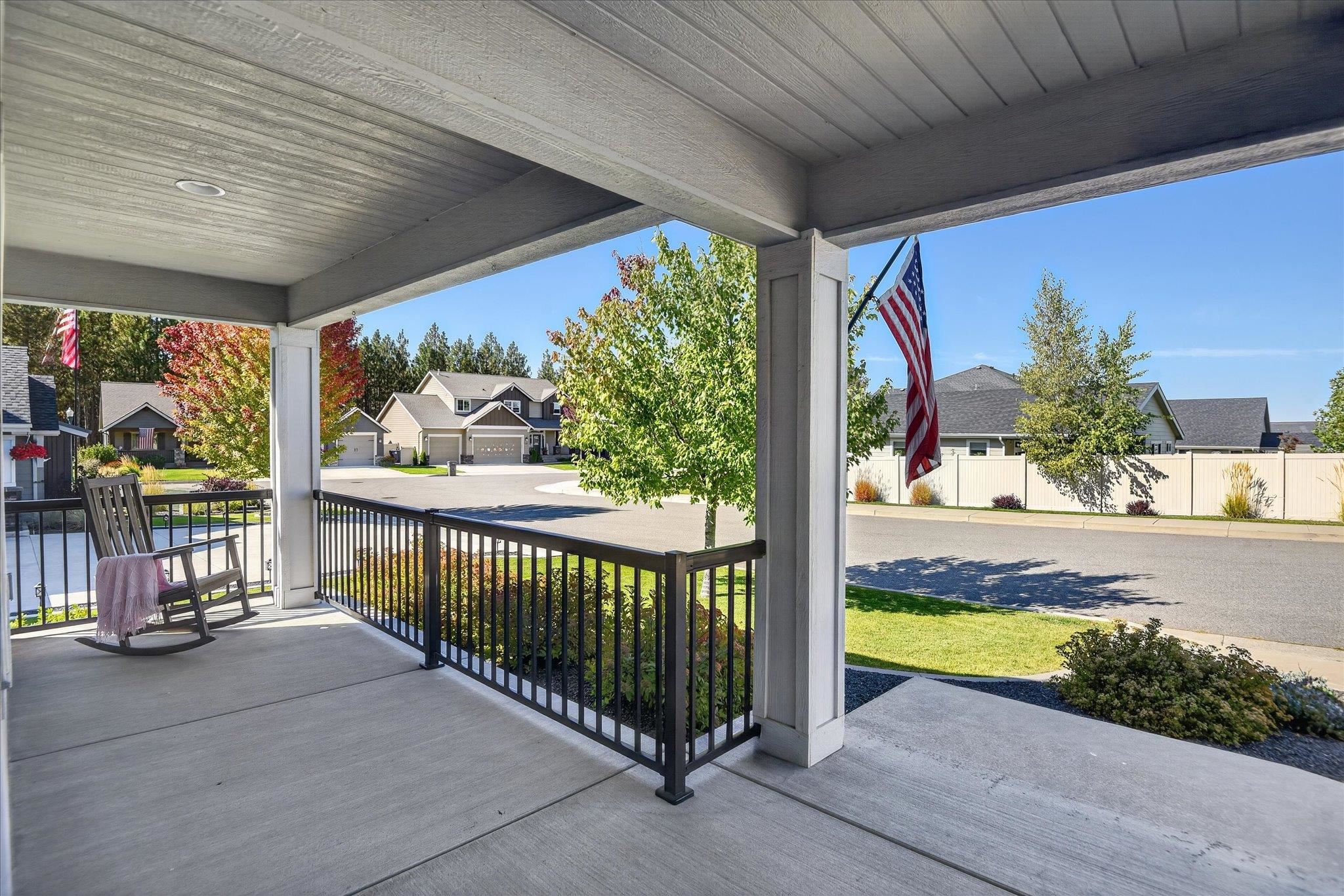 Covered front porch with a rocking chair, black railing, and an American flag overlooking the neighborhood.