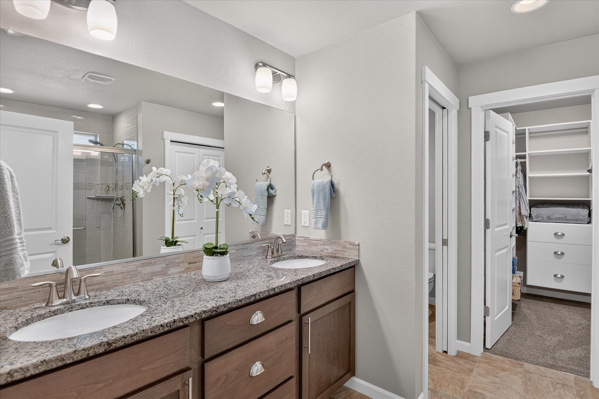 Bathroom with double-sink granite vanity, mirrored wall, and doorway to a built-in closet.