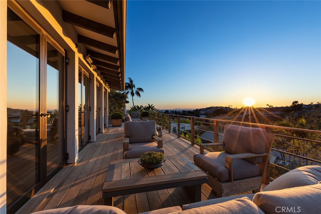 Furnished wooden deck overlooking the ocean at sunset, with cushioned chairs and a low table.