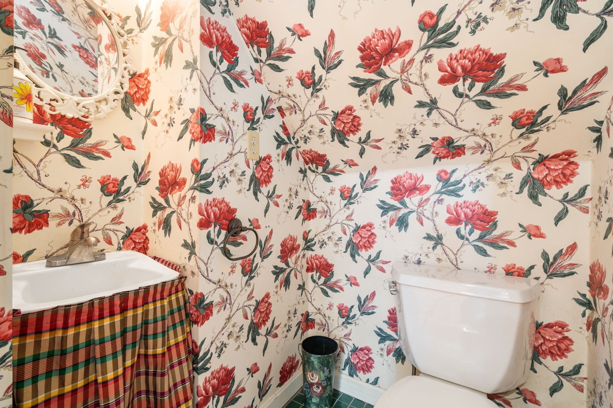 Bathroom with red floral wallpaper, a white toilet, and a sink covered by a multicolored plaid skirt.