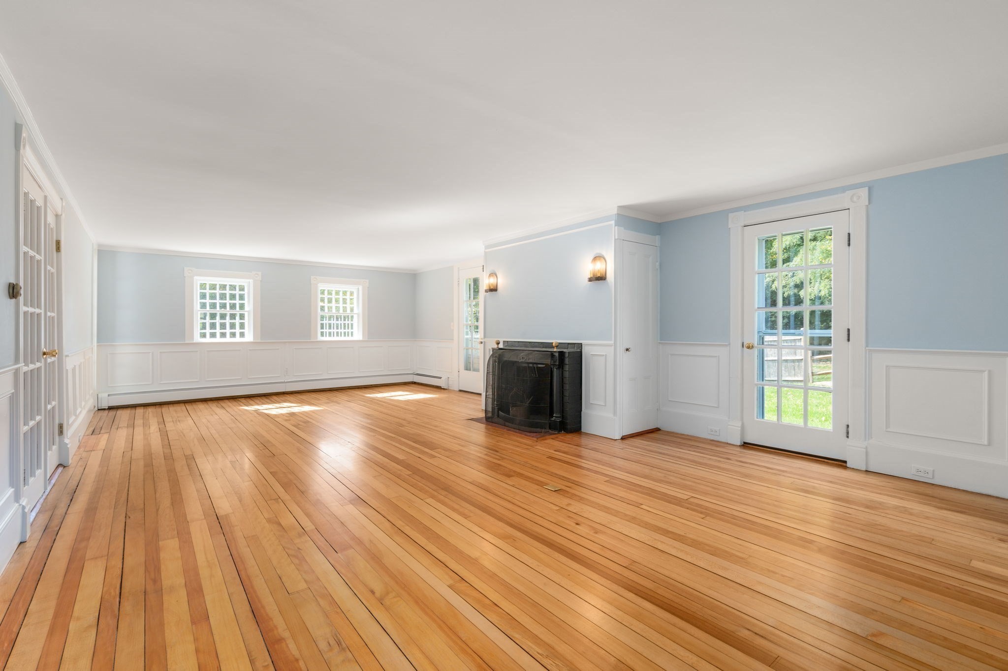 Vacant living room with hardwood floors, white wainscoting, and a black fireplace.