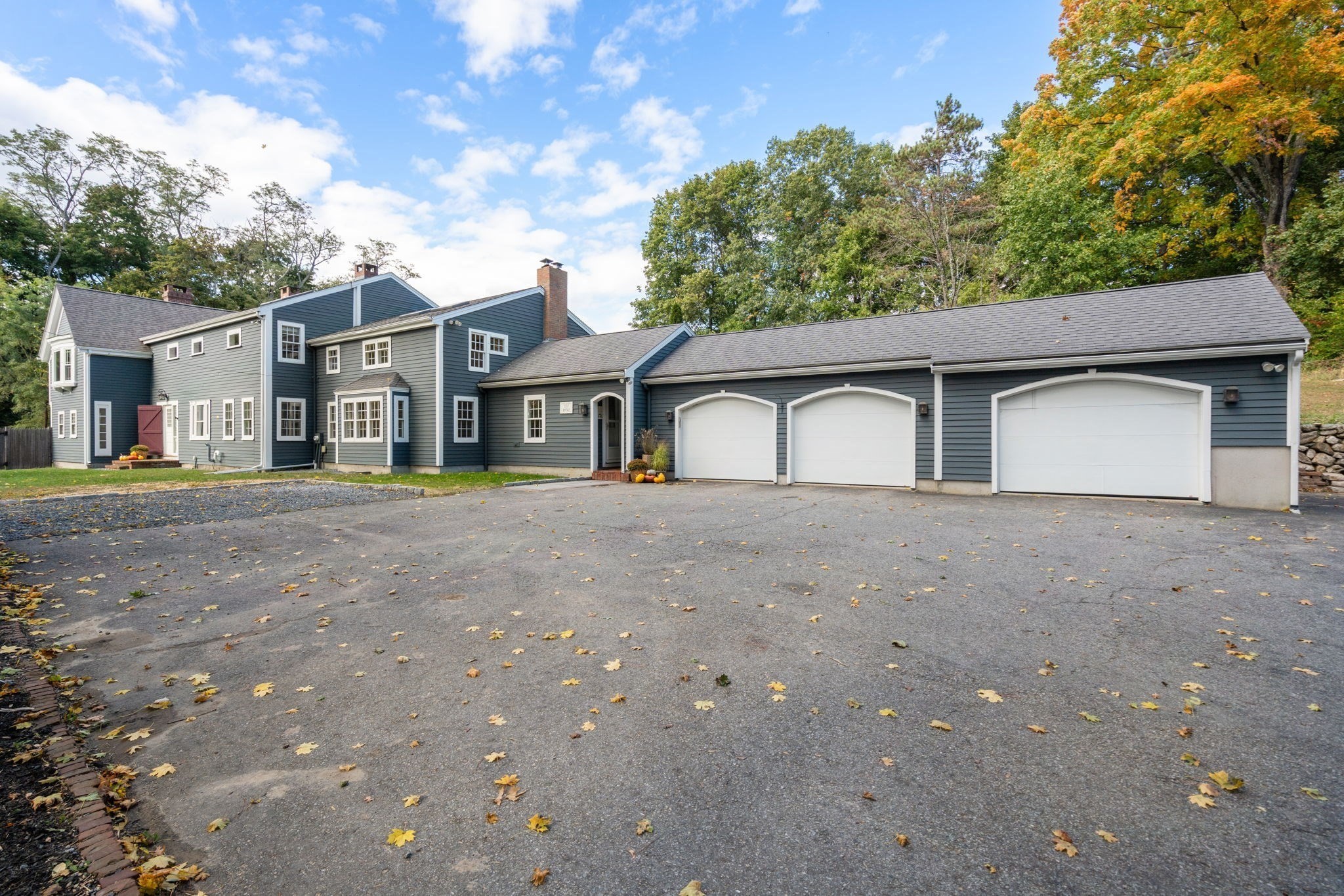 Blue-gray house with three white garage doors and a broad leaf-strewn driveway.