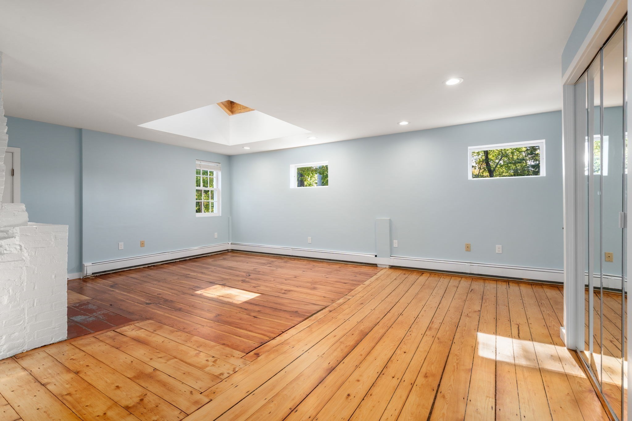 Vacant room with wide-plank wood floors, pale blue walls, and a skylight.