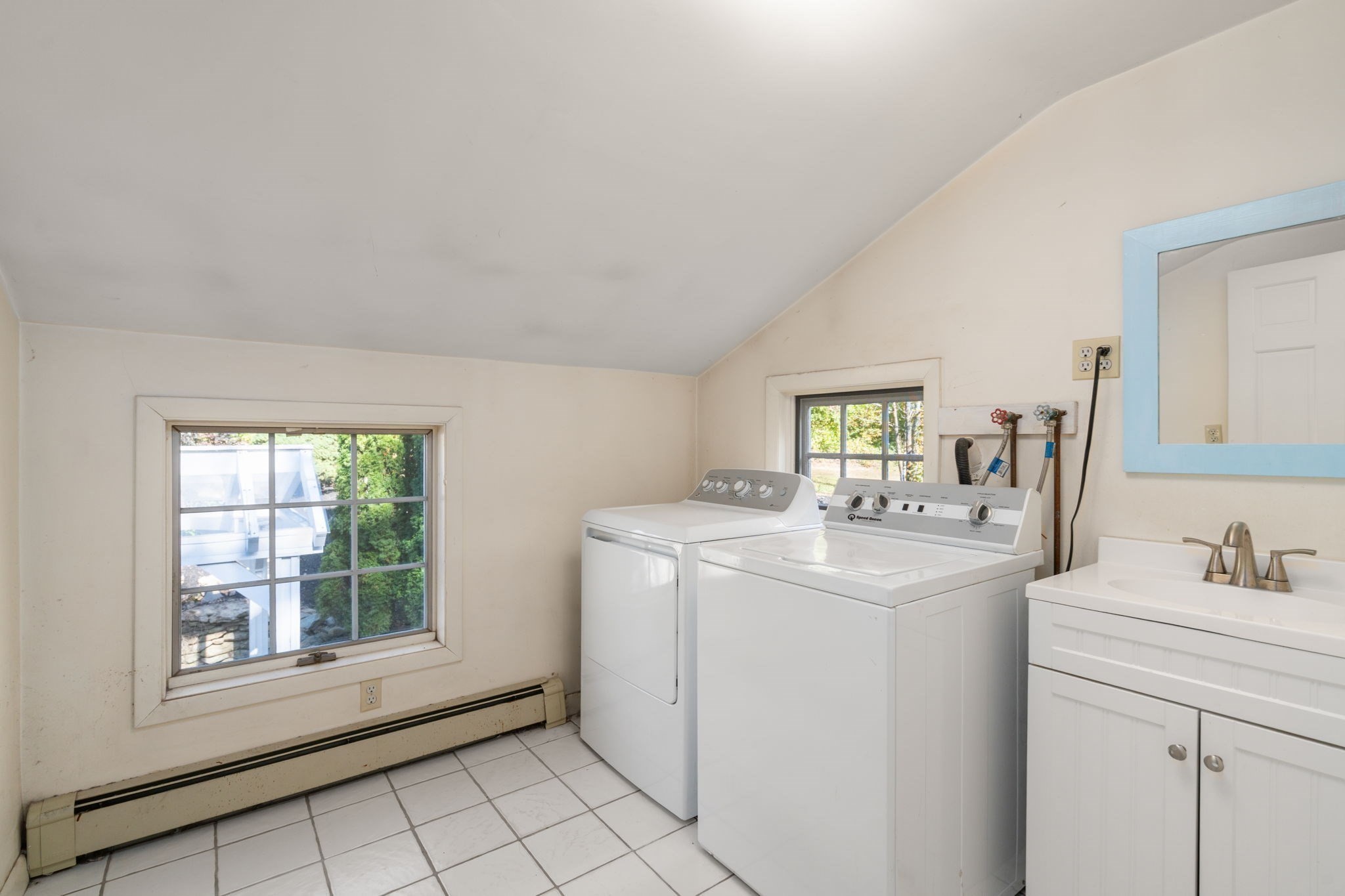 Laundry room with a top-loading washer and dryer, utility sink, and two windows.