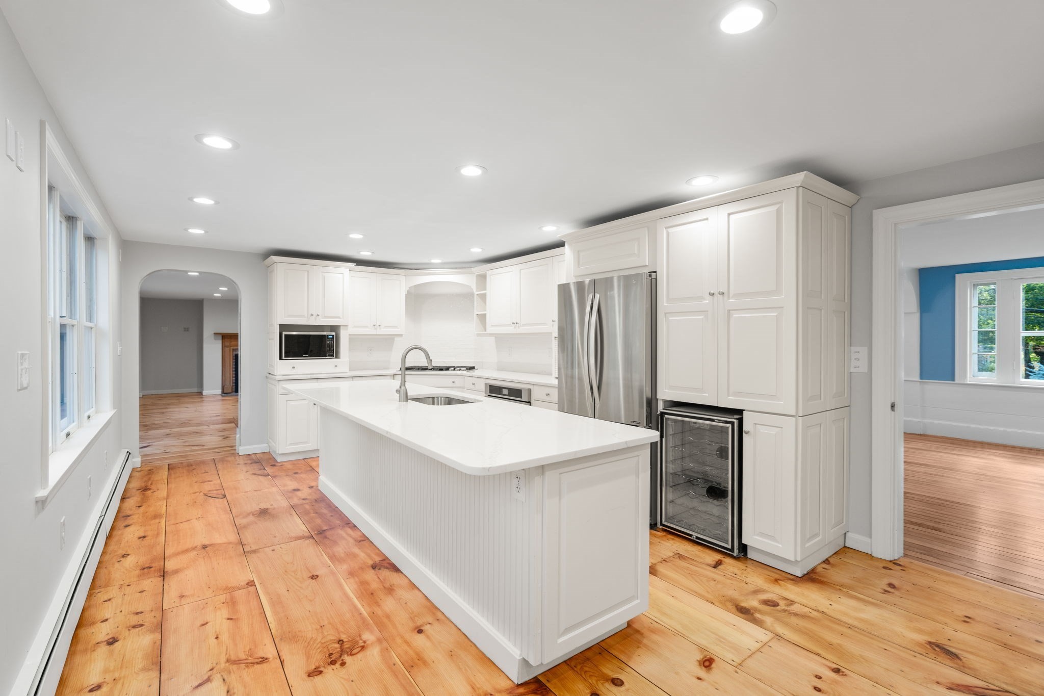 Bright white kitchen with a large island, stainless steel appliances, and wide-plank wood floors.