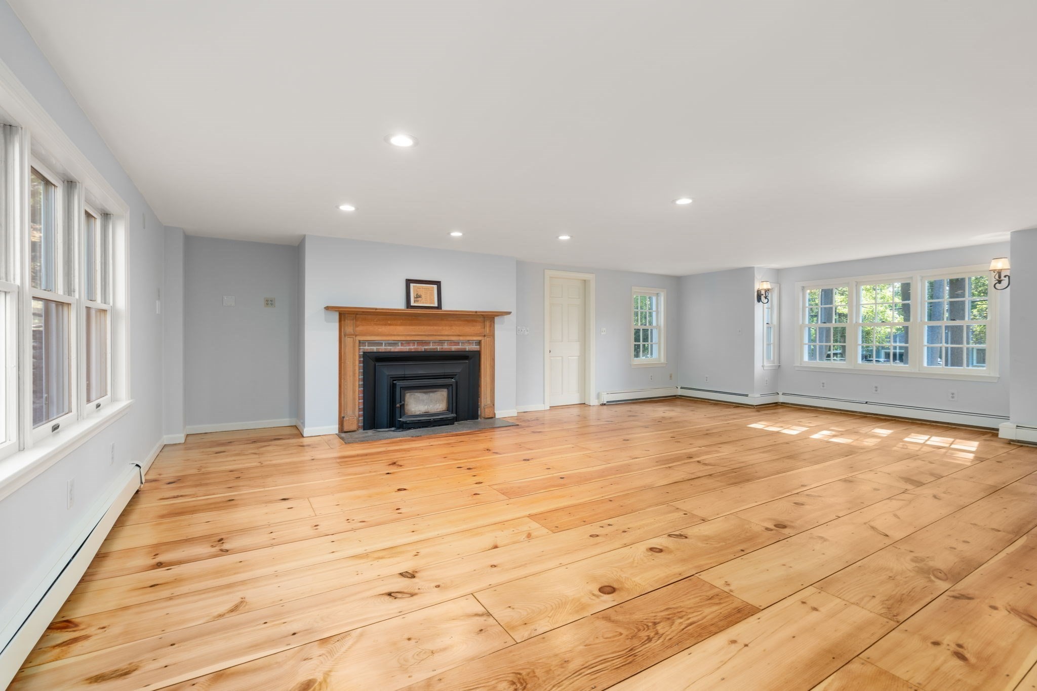 Vacant living room with wide plank floors, a wood-trimmed fireplace, and large windows.