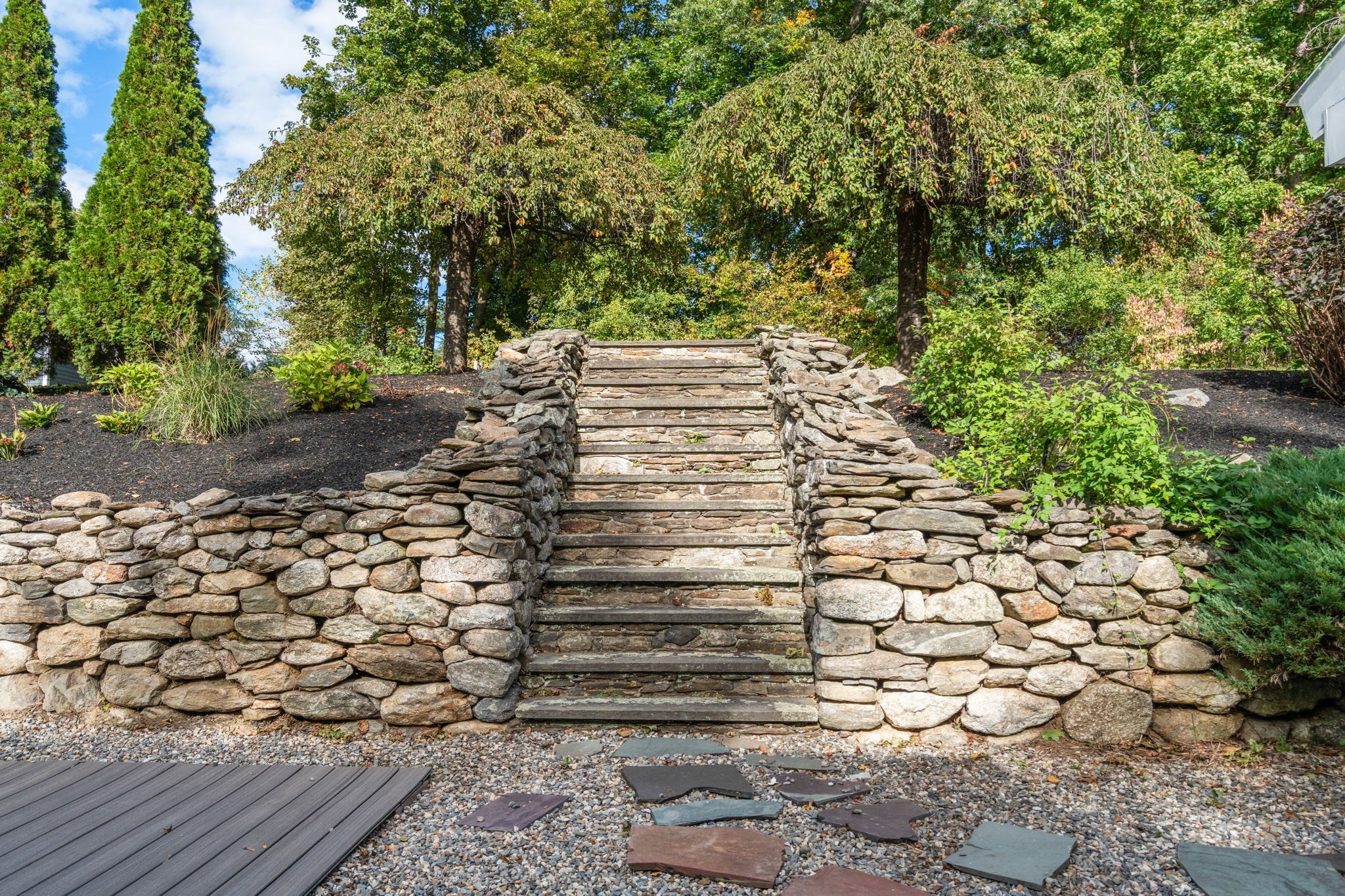 Stone steps climb between stacked-stone retaining walls in a landscaped yard.