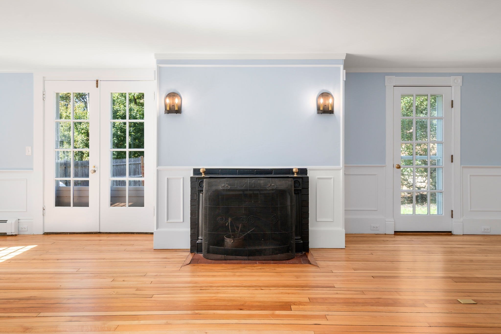 Unfurnished living room with a black fireplace between French doors and warm hardwood floors.
