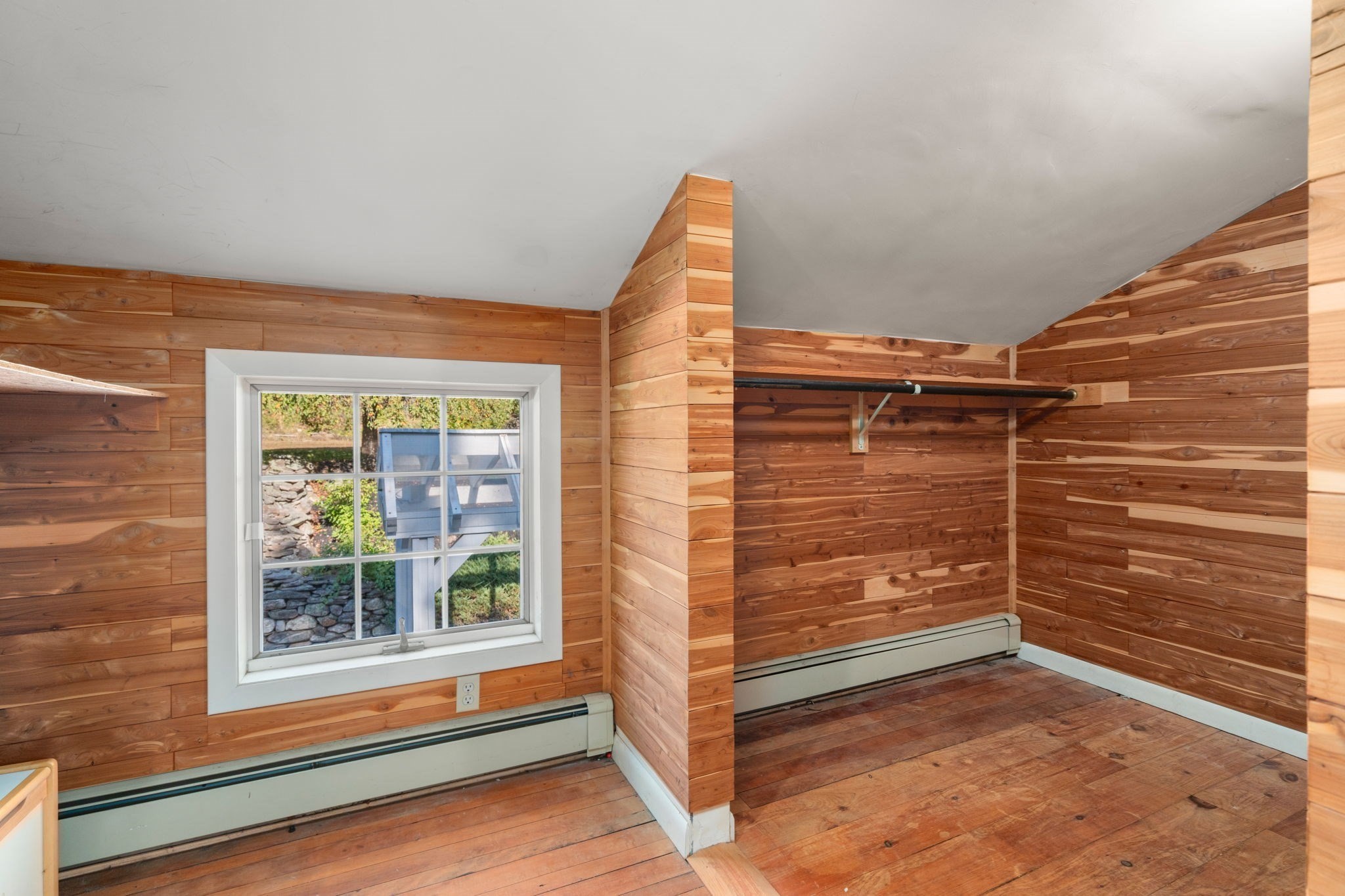 Empty wood-paneled room with a sloped ceiling, hanging rod, hardwood floor, and window.