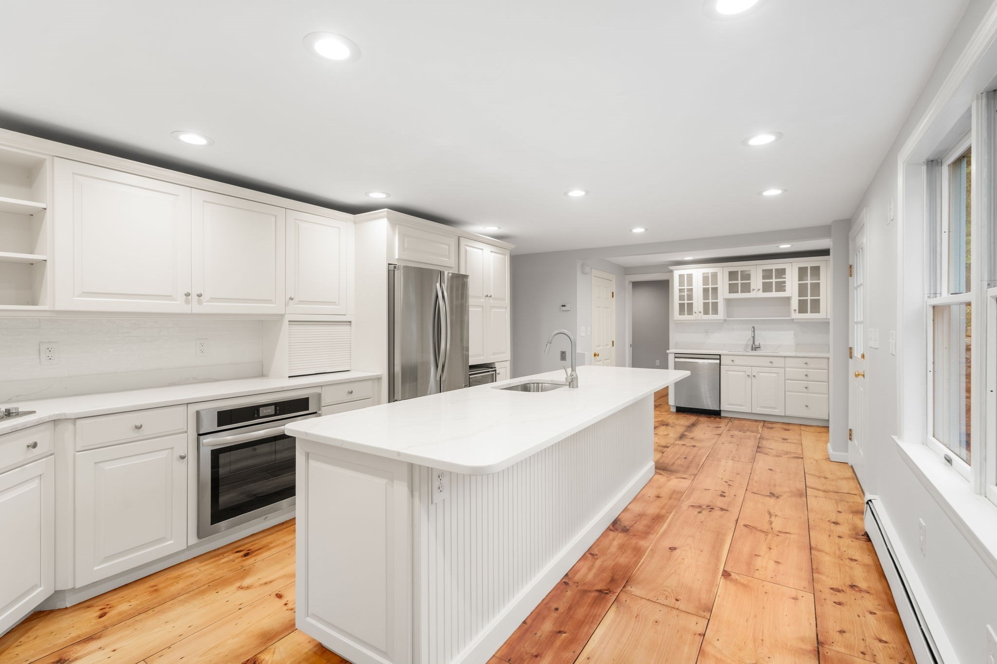 Bright white kitchen with a large island, stainless steel appliances, and wide-plank wood flooring.