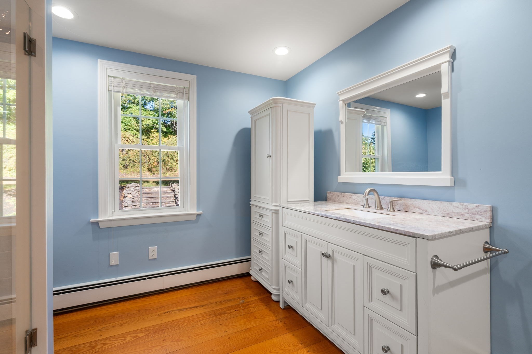 Bathroom with a white paneled vanity and large mirror against pale blue walls.