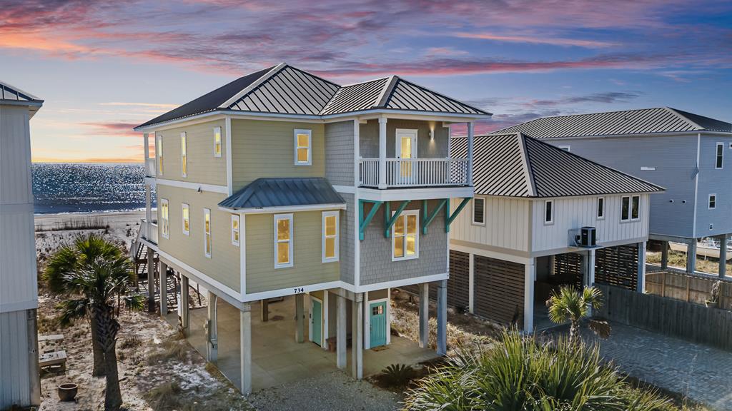Elevated coastal beach house with a metal roof and ocean visible behind it.