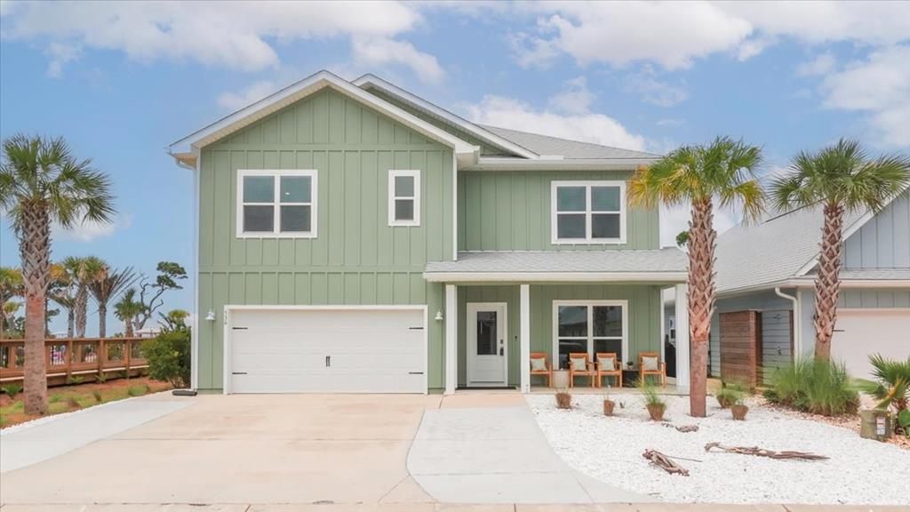 Sage-green two-story coastal home with a double garage, furnished porch, and palm trees.