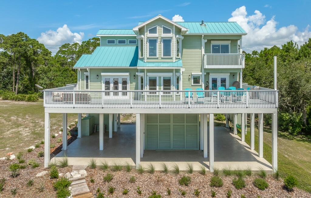 Raised pale-green coastal home with a broad white deck and covered parking below.