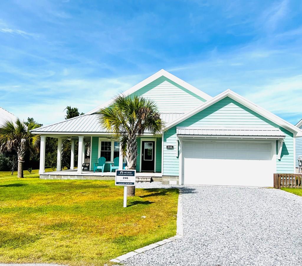 Turquoise coastal house with a covered porch, palm trees, and a gravel driveway.