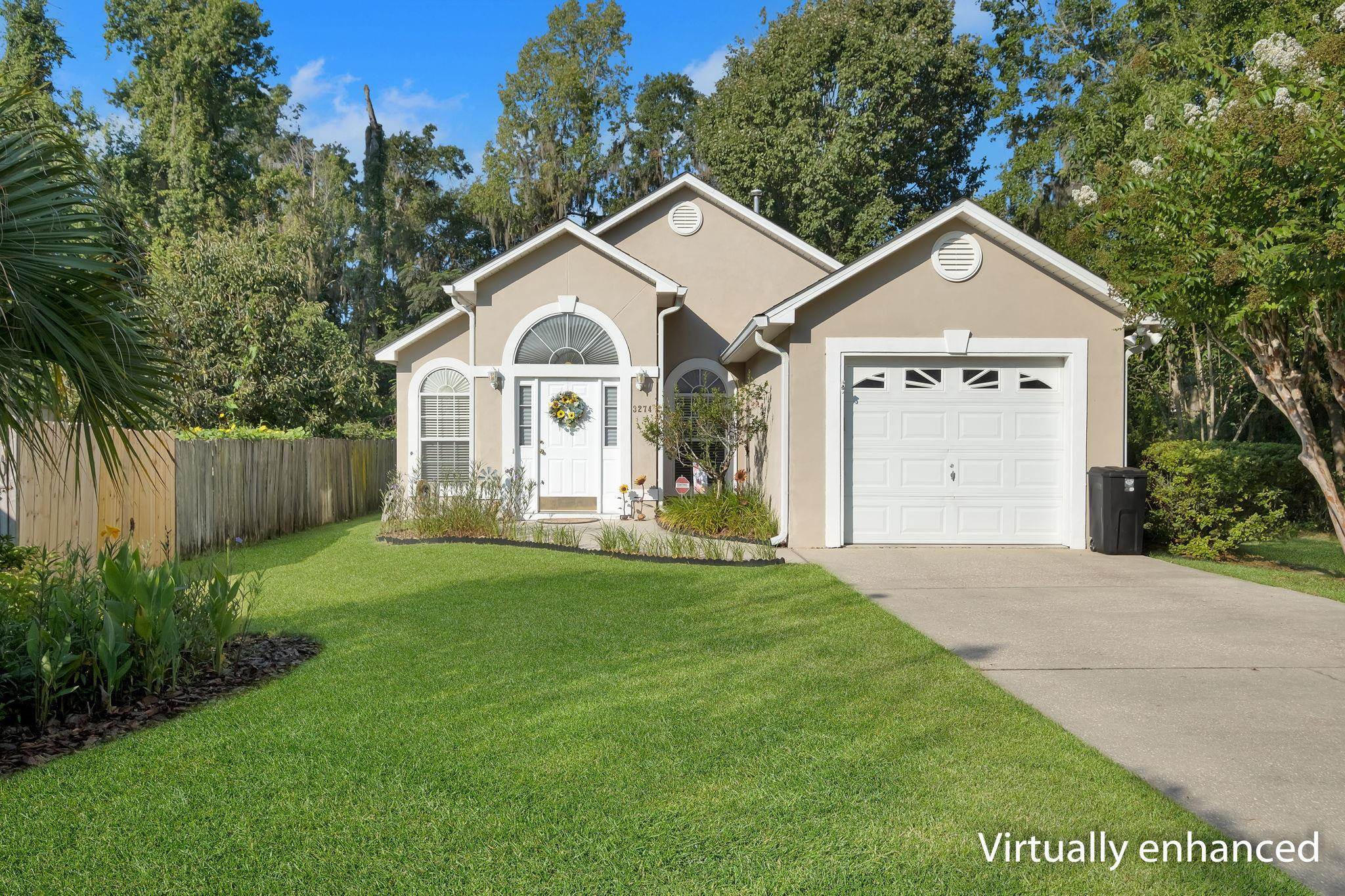 Beige house with arched windows, white entry door, attached garage, and a broad green lawn.