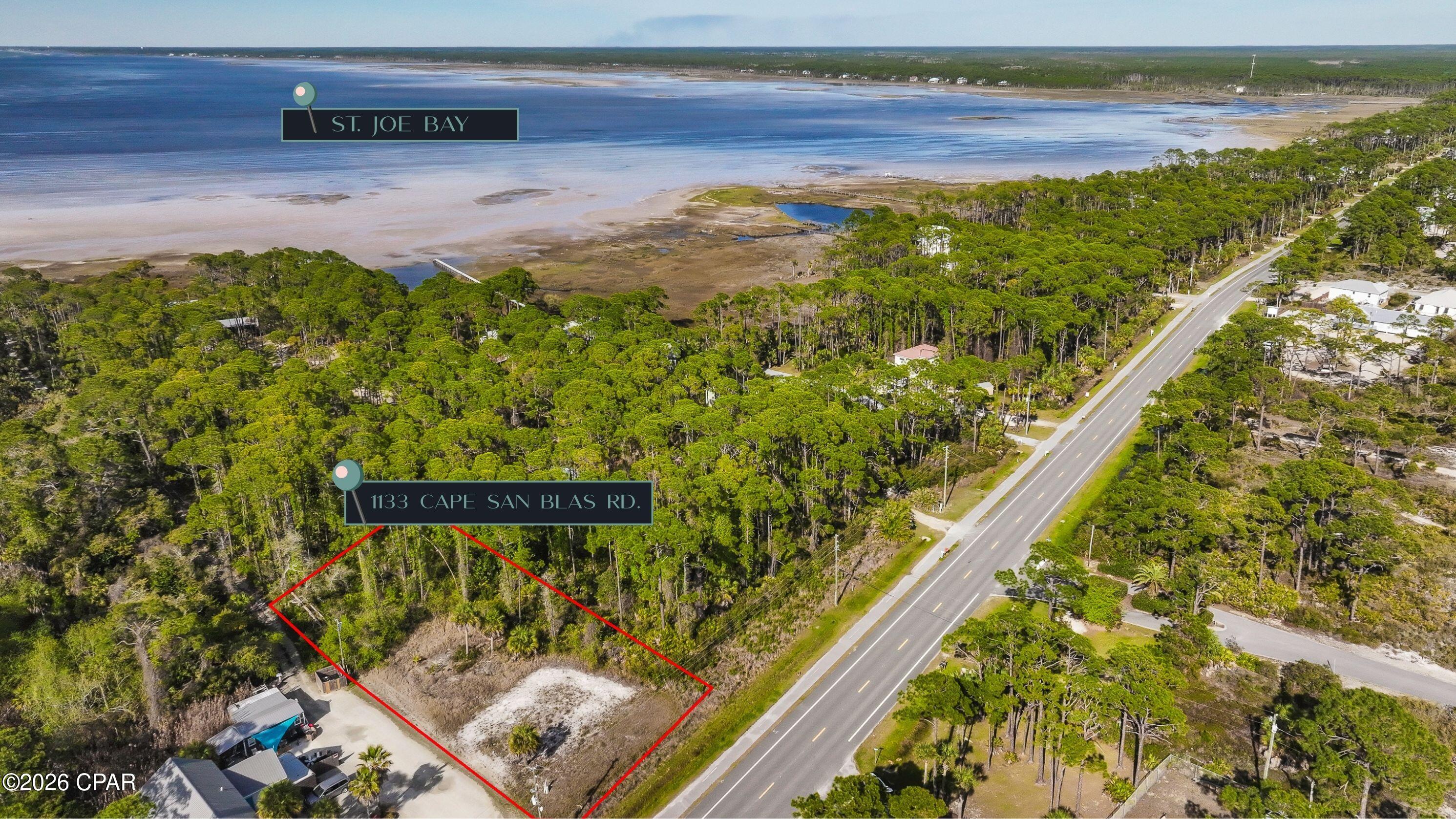 Aerial view of a wooded vacant lot outlined in red beside Cape San Blas Road, with St. Joe Bay beyond.