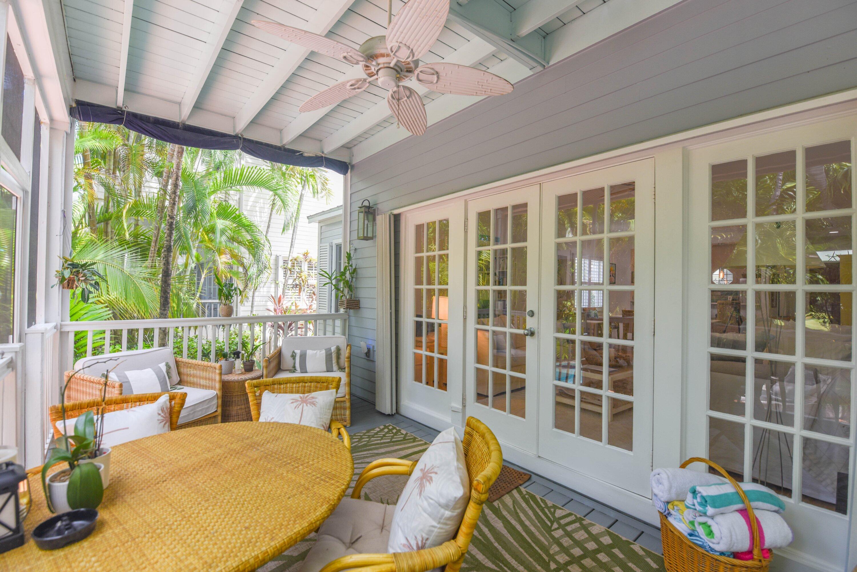 Covered porch with wicker seating, French doors, a ceiling fan, and tropical plants.