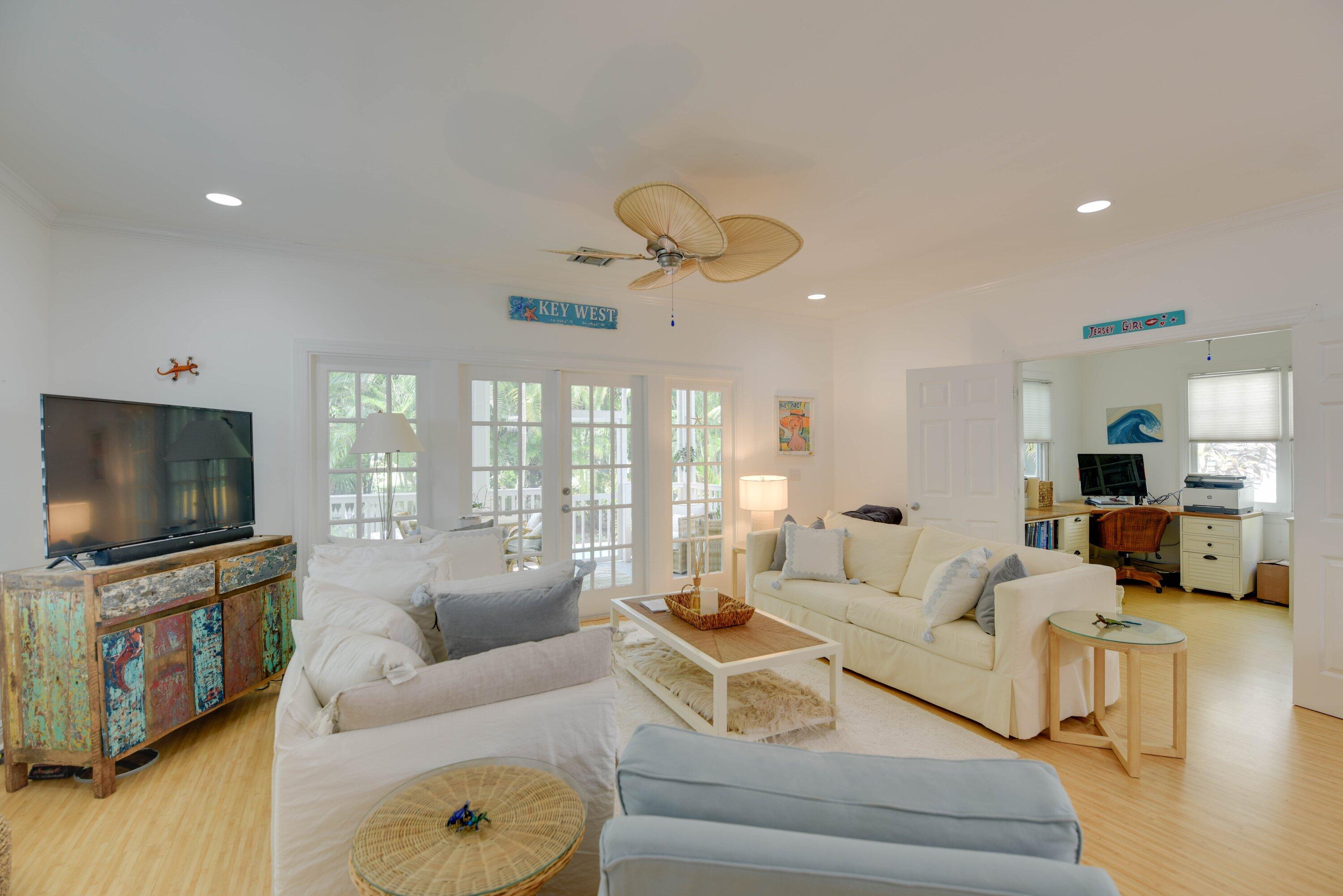 Living room with white sofas, a colorful rustic cabinet, and French doors opening to a porch.