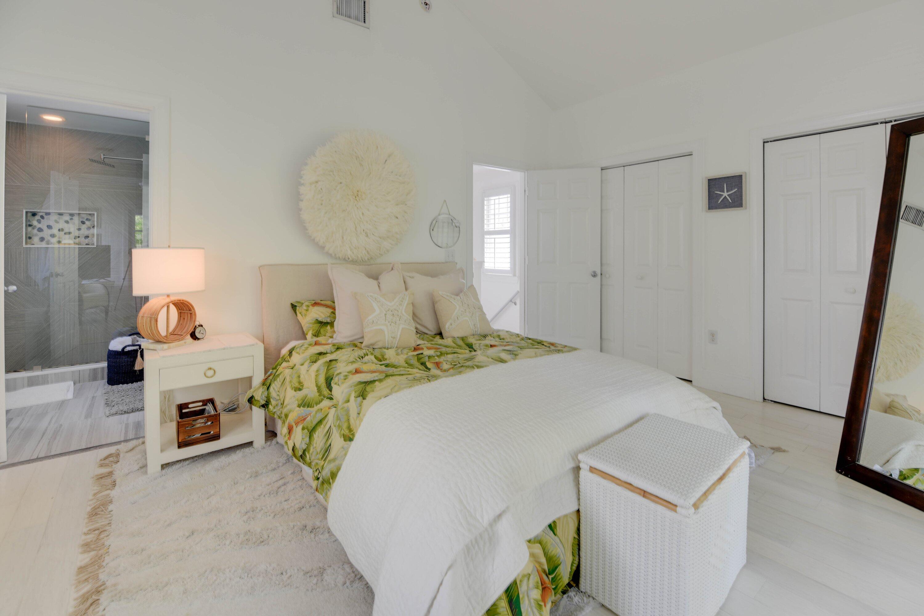 Bright bedroom with tropical leaf-patterned bedding and an ensuite bathroom visible through the doorway.