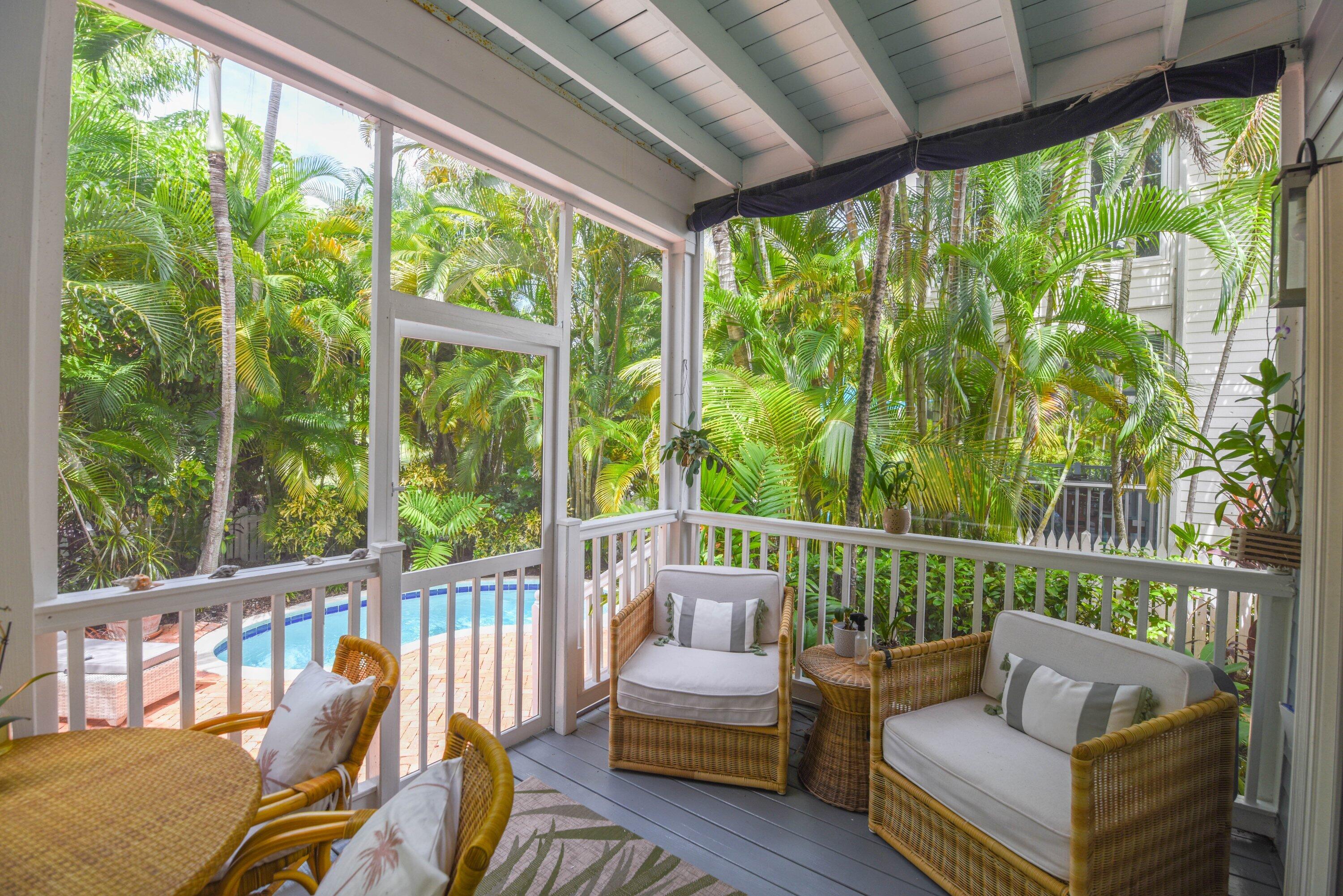 Screened porch with wicker seating overlooking a pool and tropical foliage.
