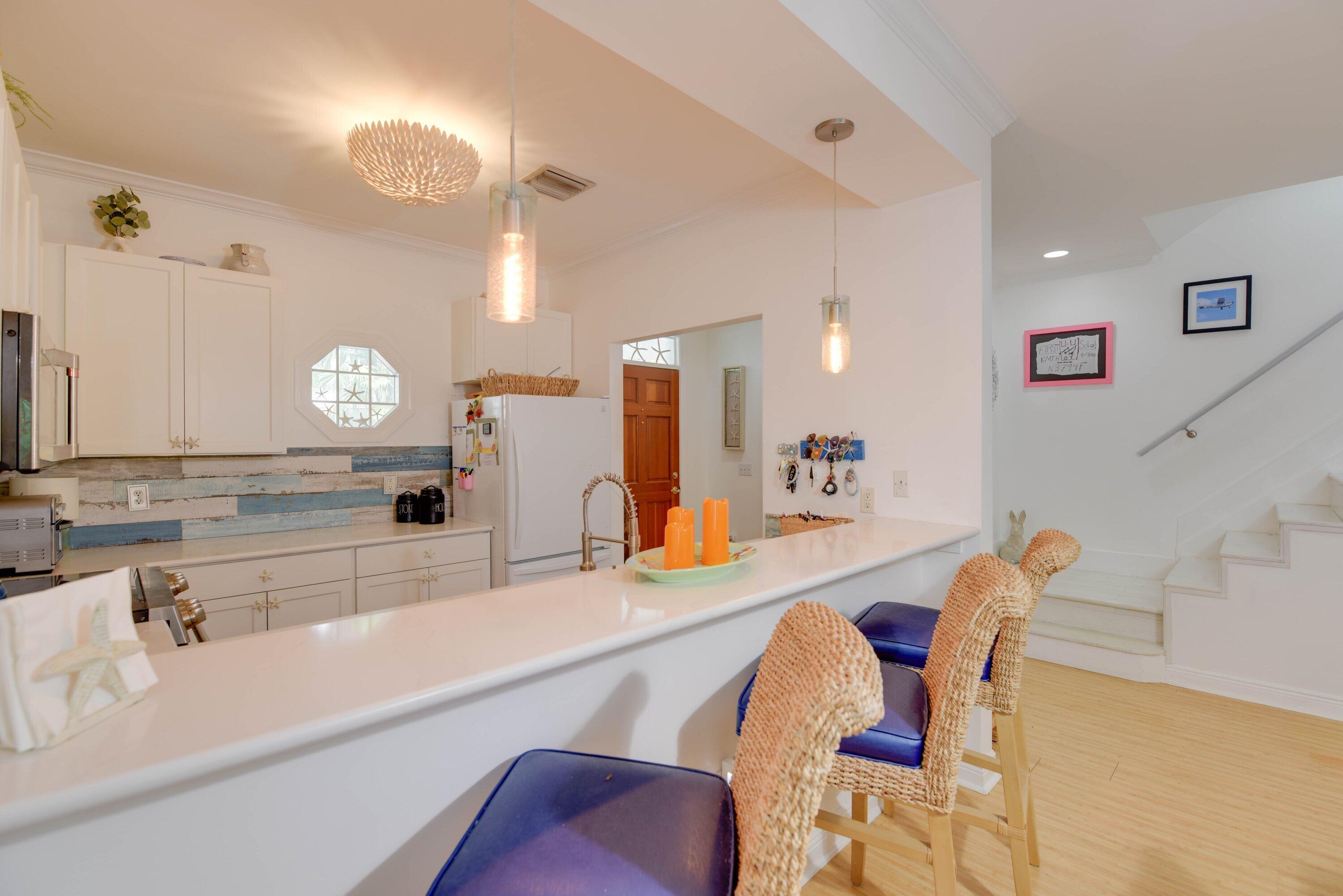Kitchen with a long white breakfast bar, woven blue-cushioned stools, and stairs alongside.
