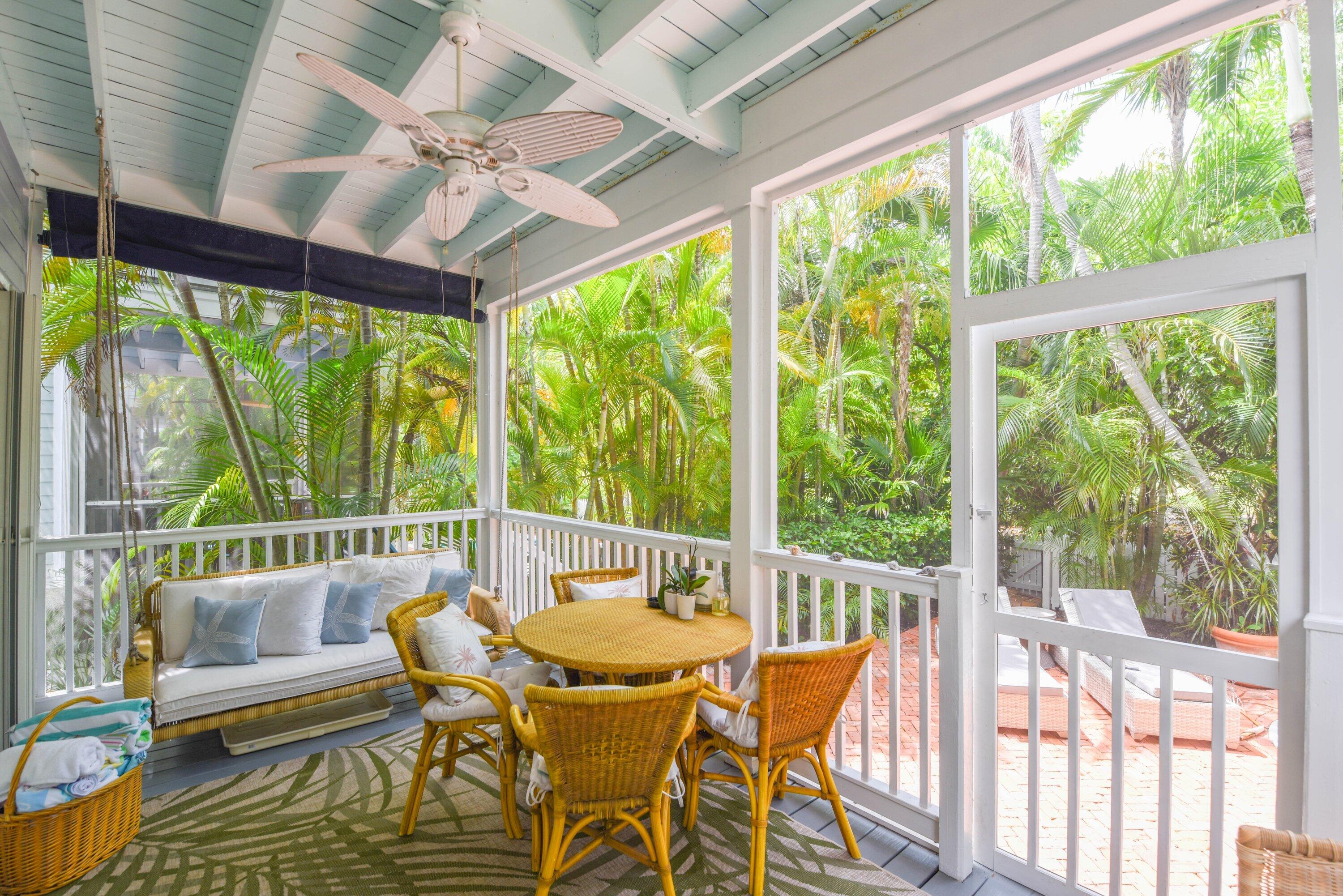 Covered porch with wicker seating and dining table overlooking a lush tropical garden.