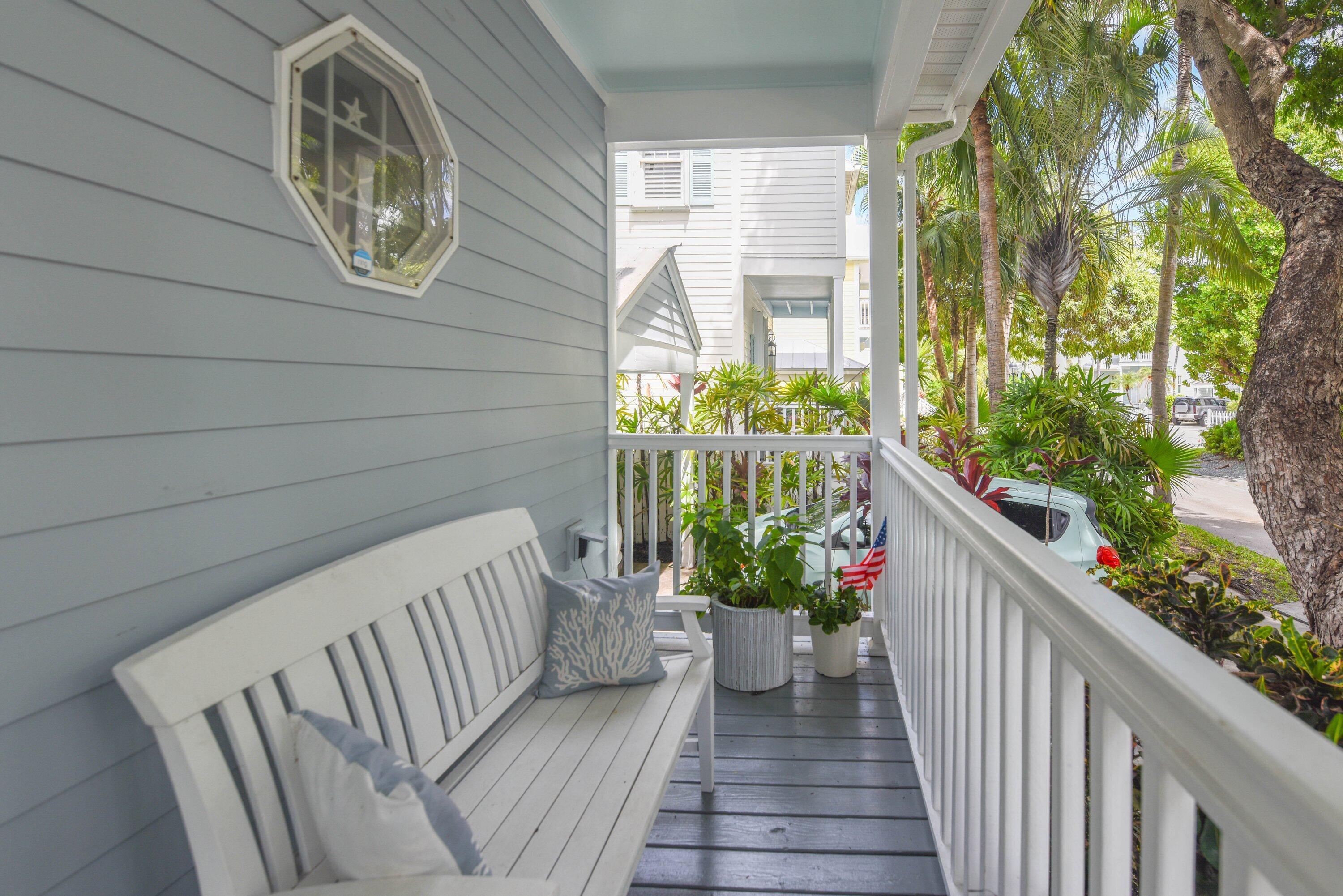 Furnished porch with a white bench, potted tropical plants, and an octagonal window.