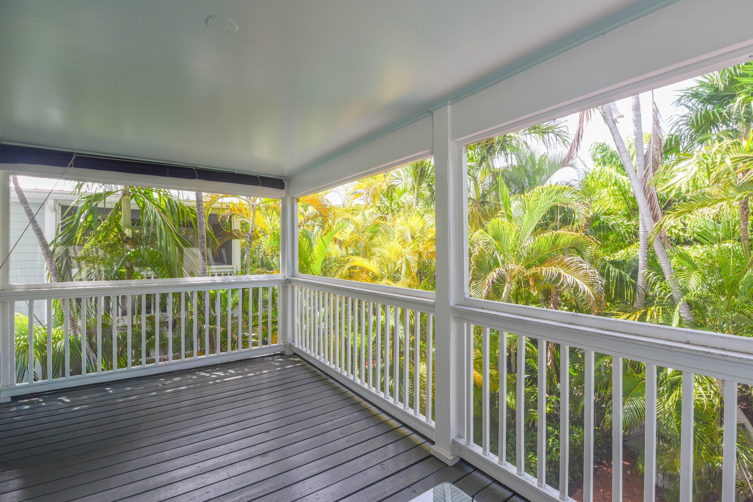 Covered porch with gray decking and white railings overlooking dense tropical palms.