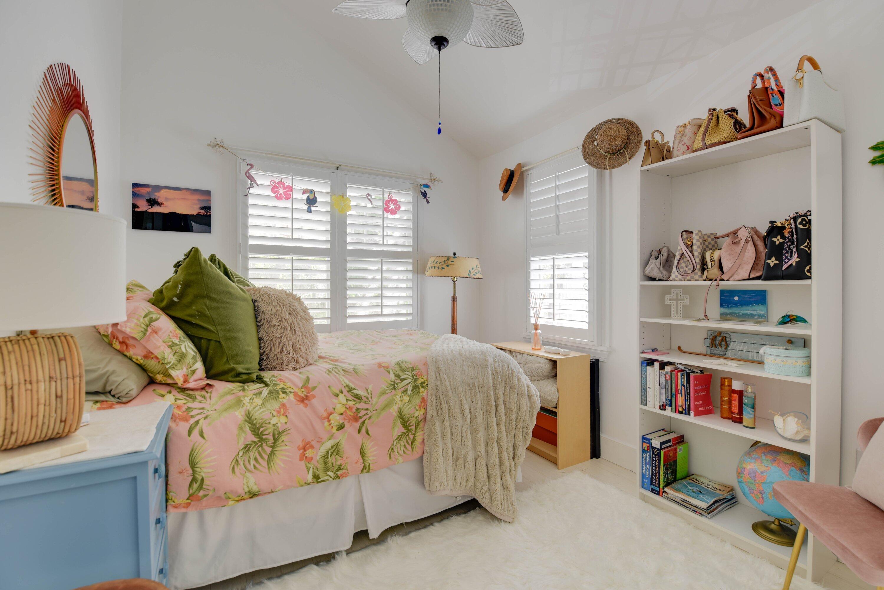 Bright bedroom with tropical floral bedding, plantation shutters, and a built-in bookshelf.