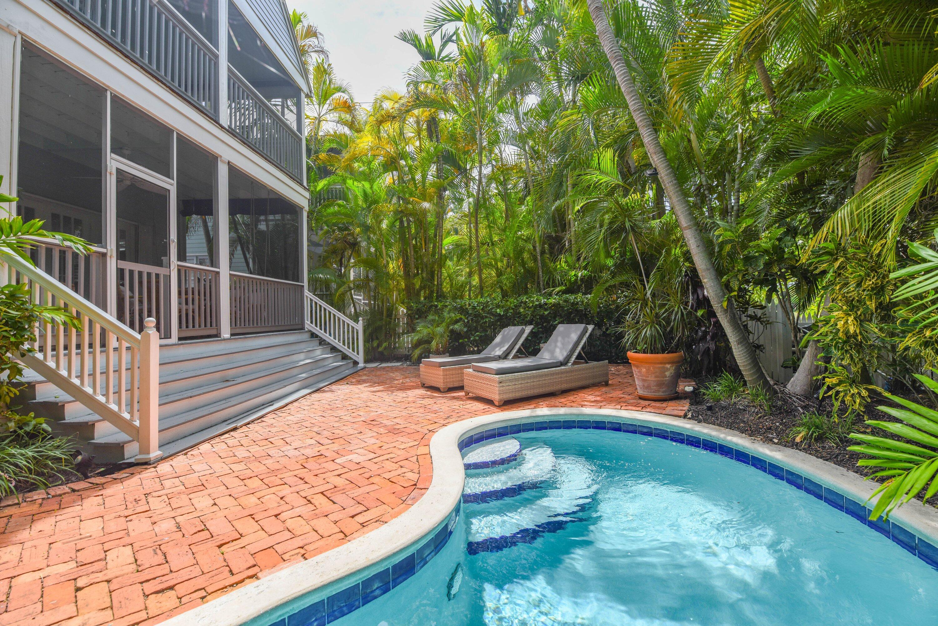 Curved pool beside a screened porch, with a brick patio and tropical landscaping.